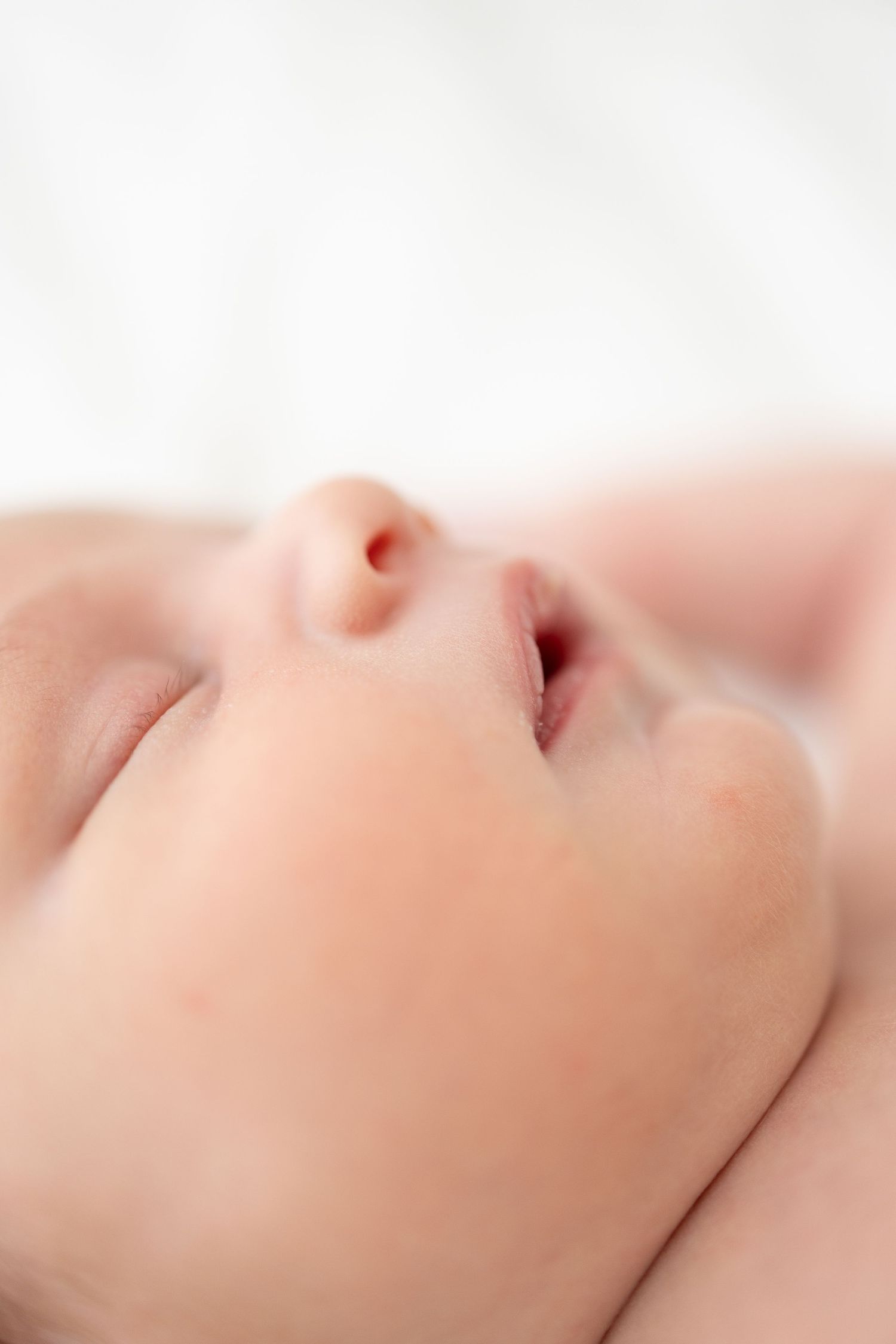 Macro close-up of a peaceful sleeping baby's nose and mouth against a soft white background.