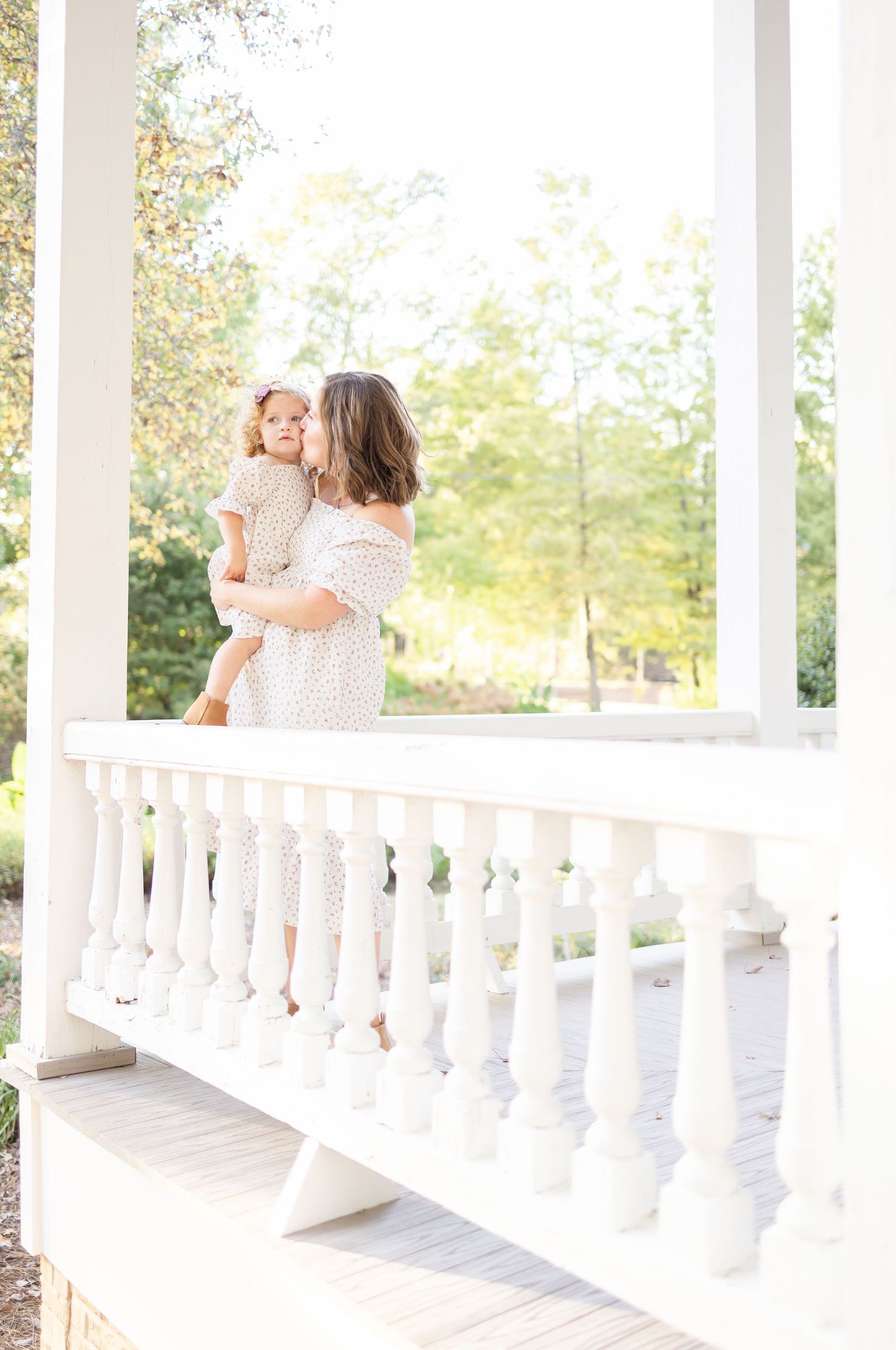 A touching moment captured on a white gazebo porch with soft natural lighting and white balustrades.