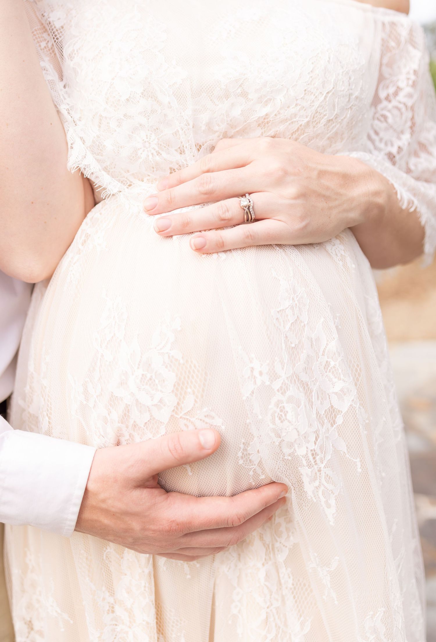 Close-up of hands tenderly holding a delicate lace wedding dress around the waist area.
