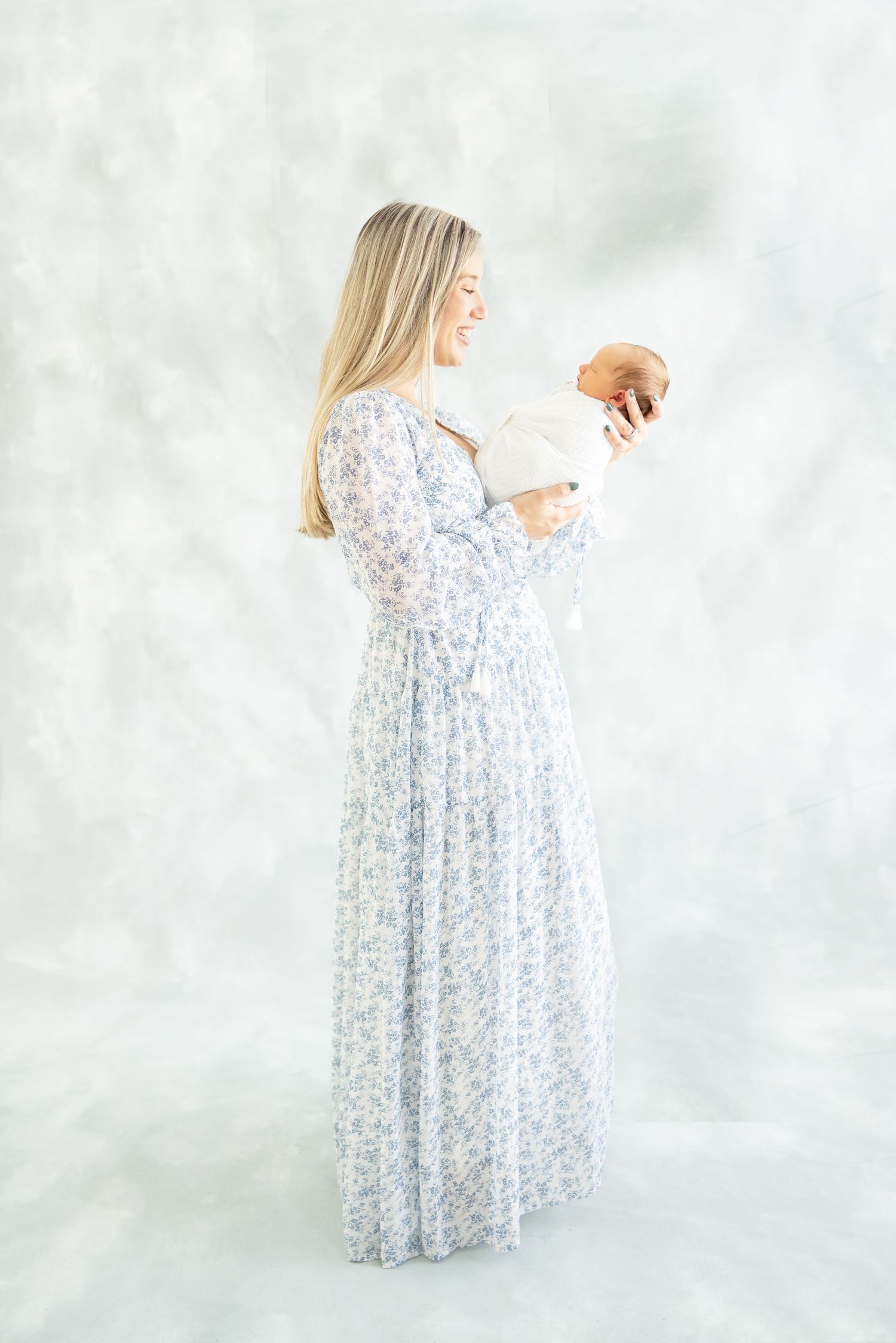 A person in a flowing floral maxi dress holds a coconut while standing against a light backdrop.