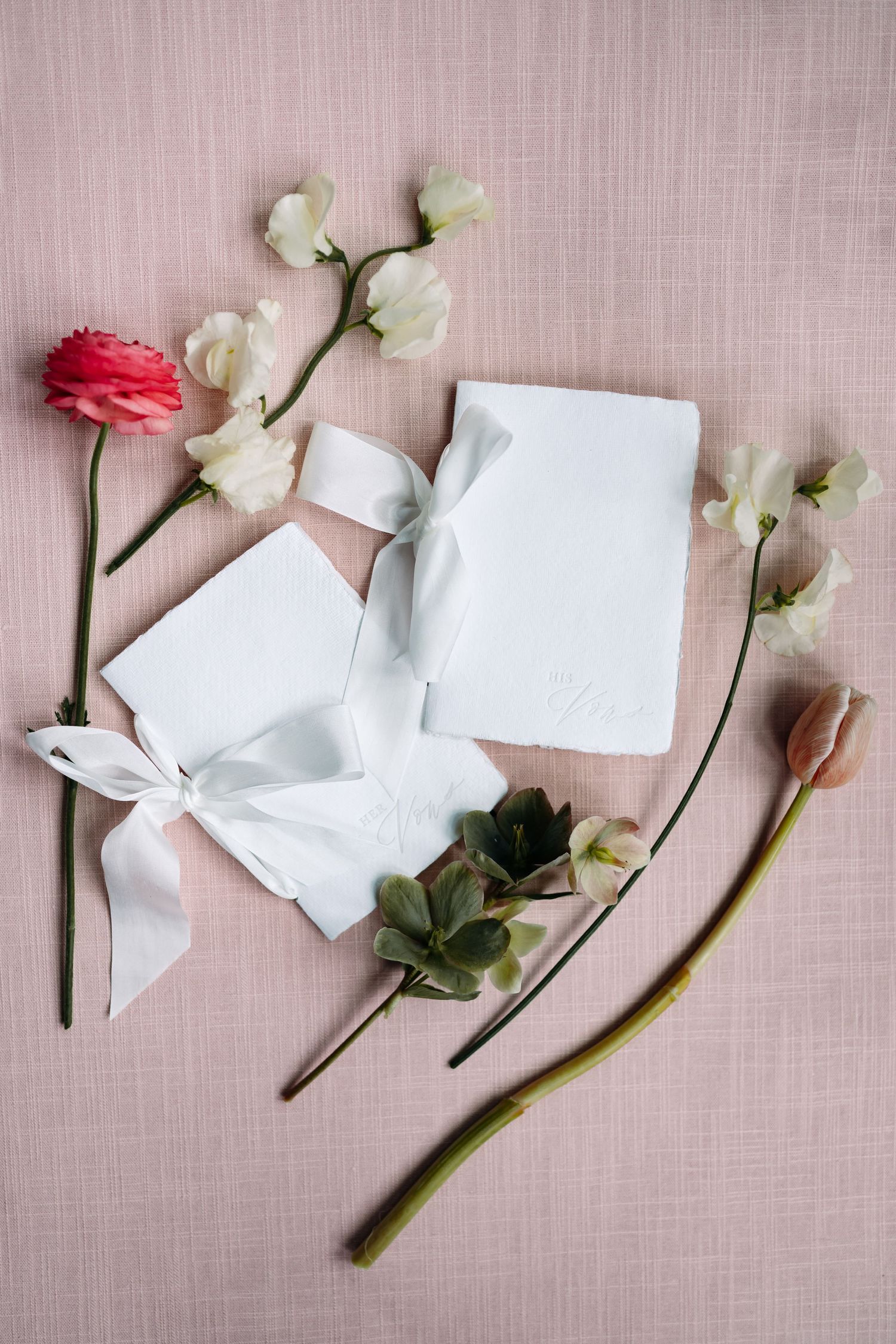 White flowers and ribbon on pink linen with blank cards for wedding stationery.