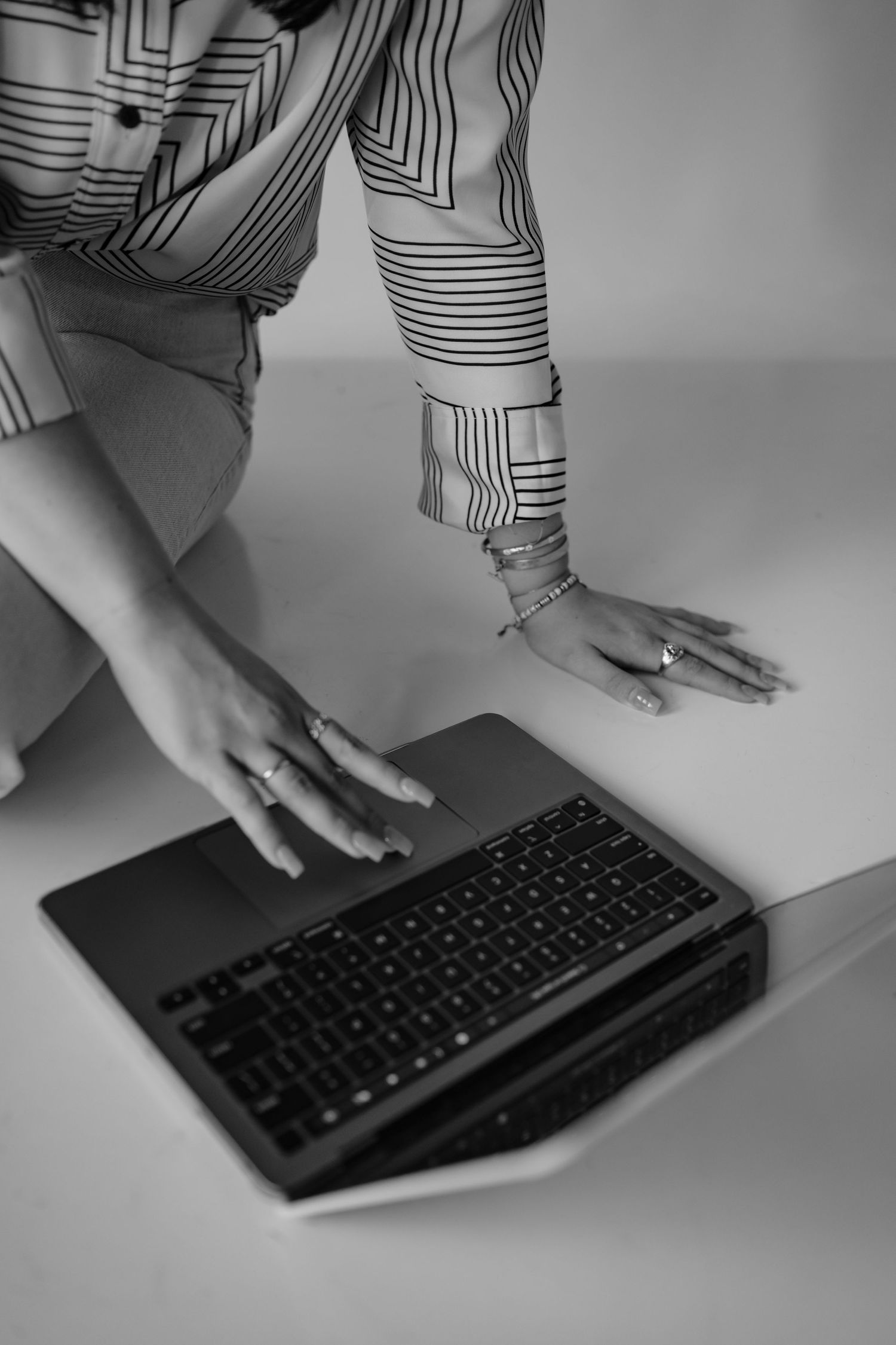 Black and white image of hands typing on a keyboard wearing a striped long sleeve shirt.