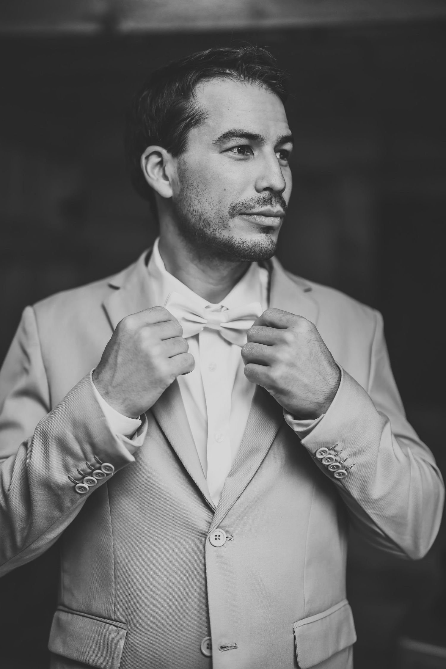 A groom in light gray suit adjusts his white bow tie before the ceremony.