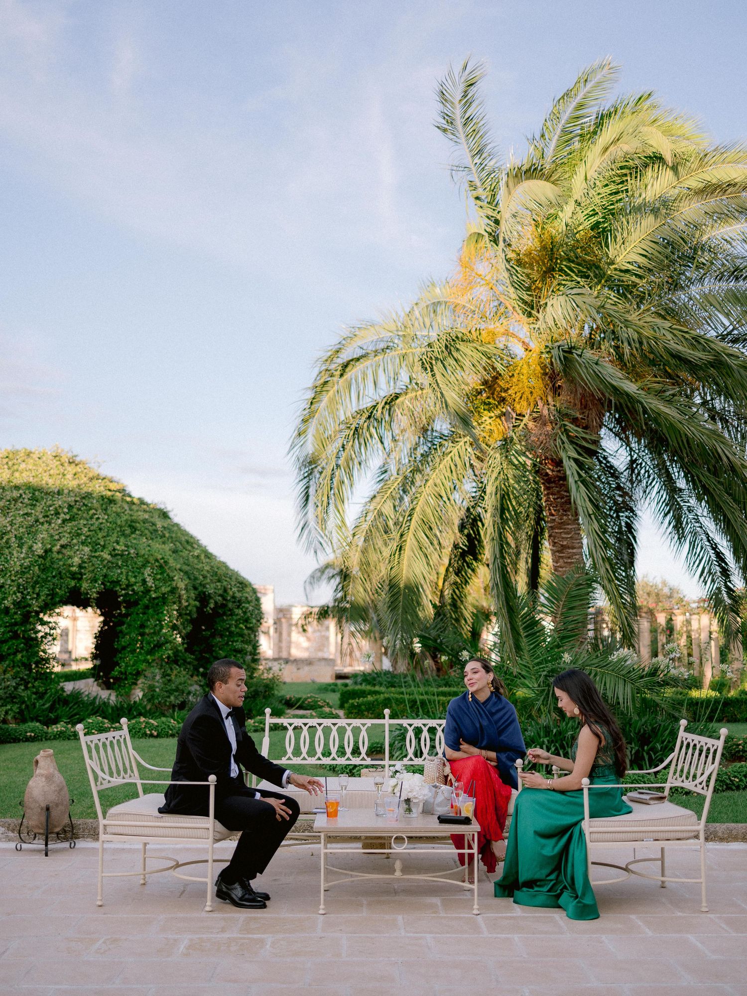 Elegant outdoor dining setup with palm trees and greenery at a Mediterranean-style terrace during golden hour.