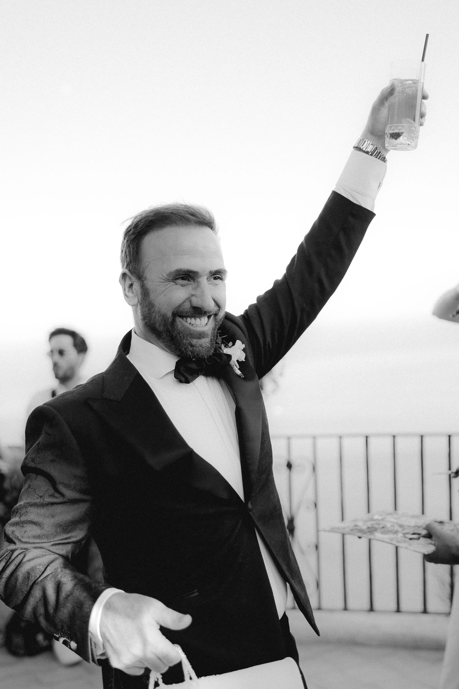 A joyful wedding celebration moment captured in black and white as a well-dressed guest raises his glass in celebration.