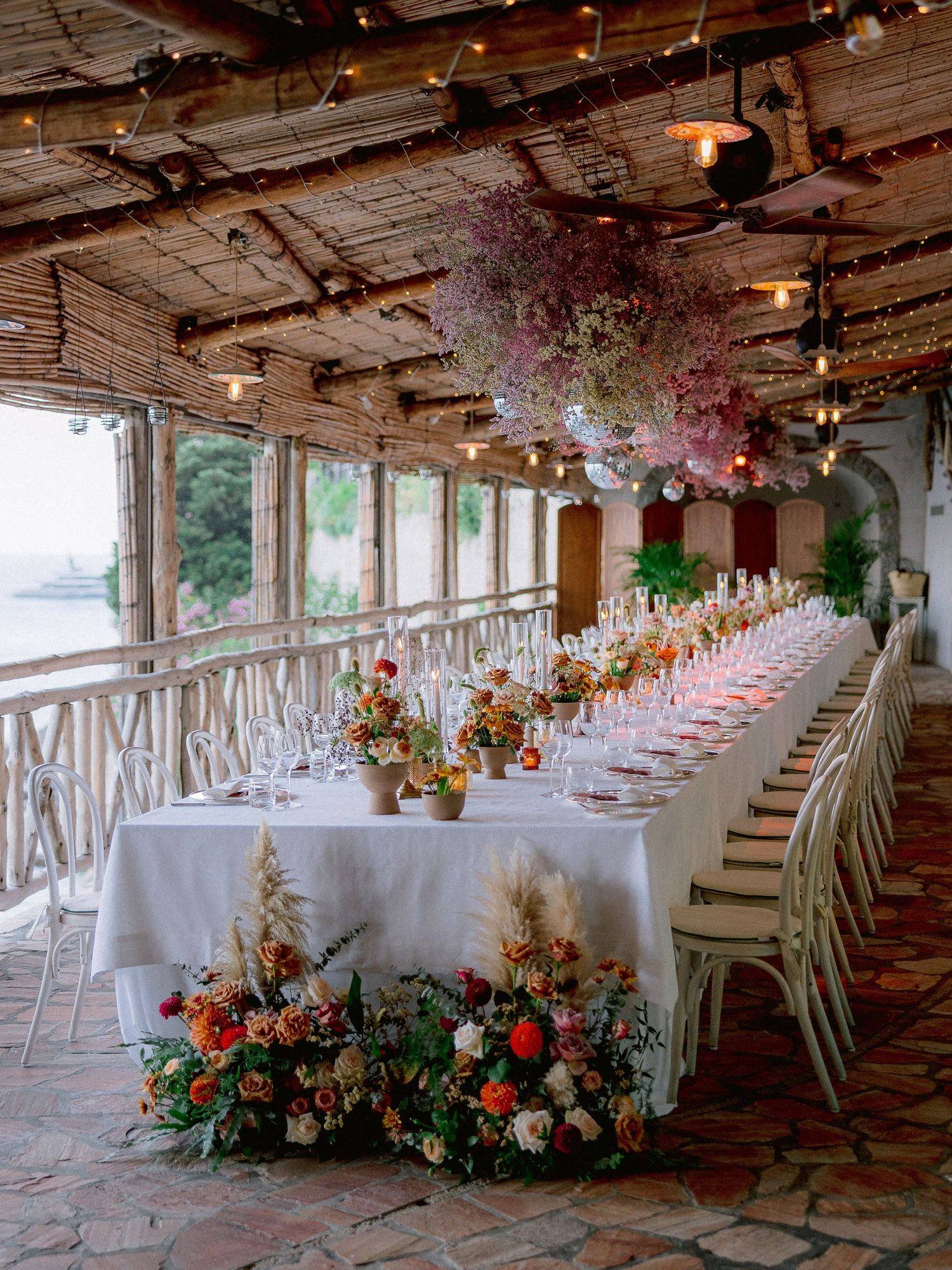 An elegant wedding reception table setup in a rustic covered porch with floral arrangements and string lights overhead.