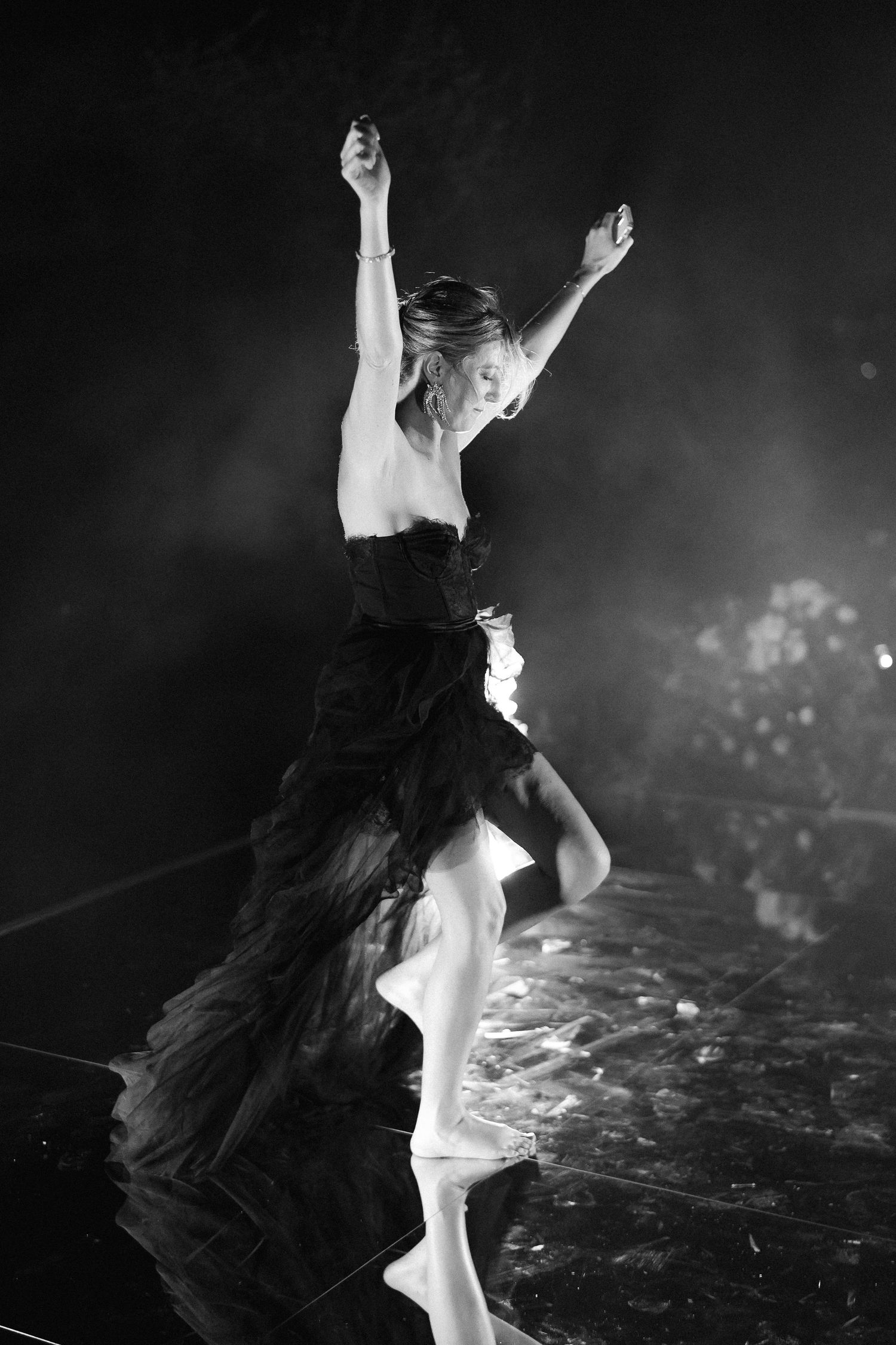 A dancer in a black and white tulle costume performs an expressive leaping movement on stage in dramatic lighting.