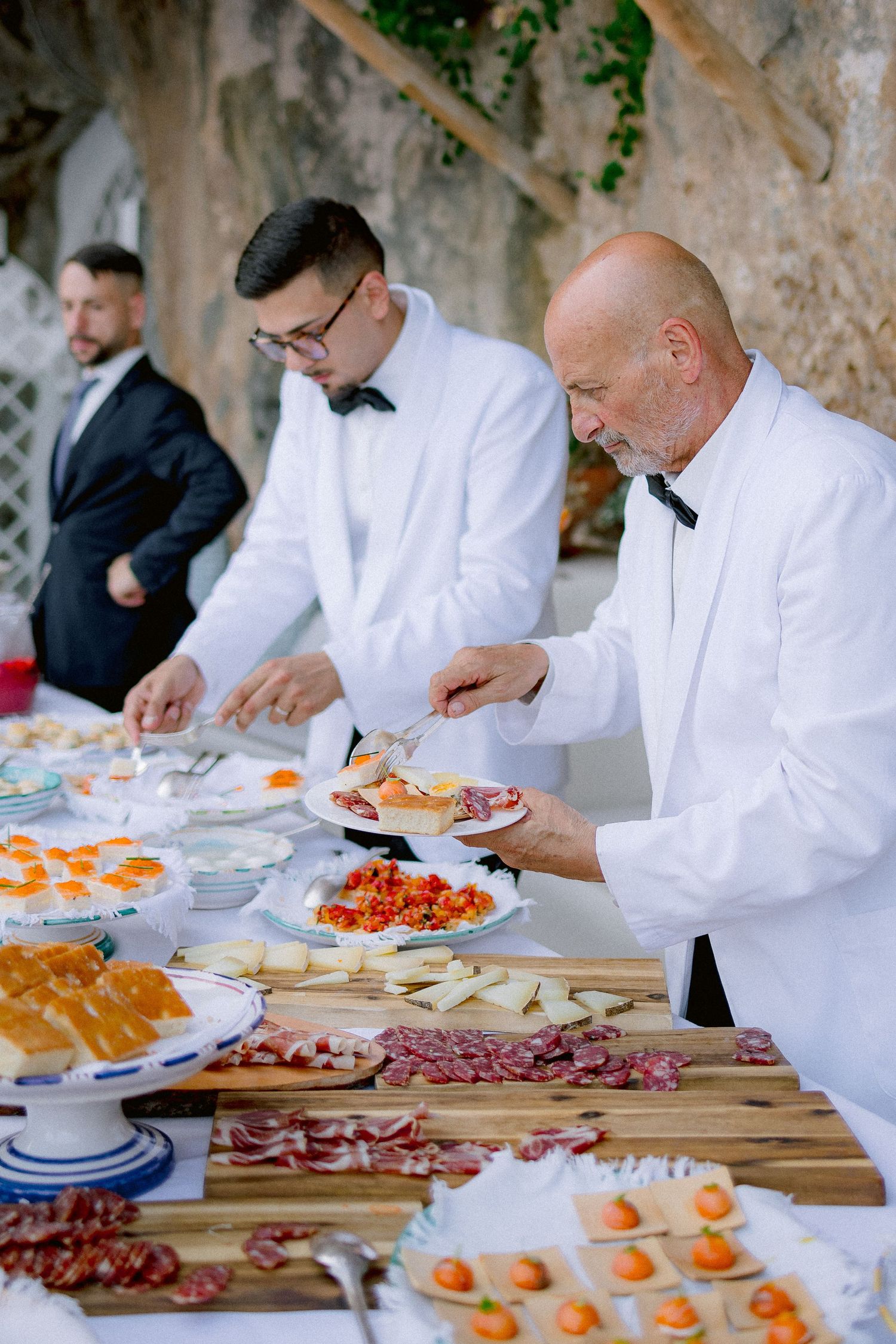 Professional catering staff in white jackets serve appetizers at an elegant buffet table with assorted hors d'oeuvres.