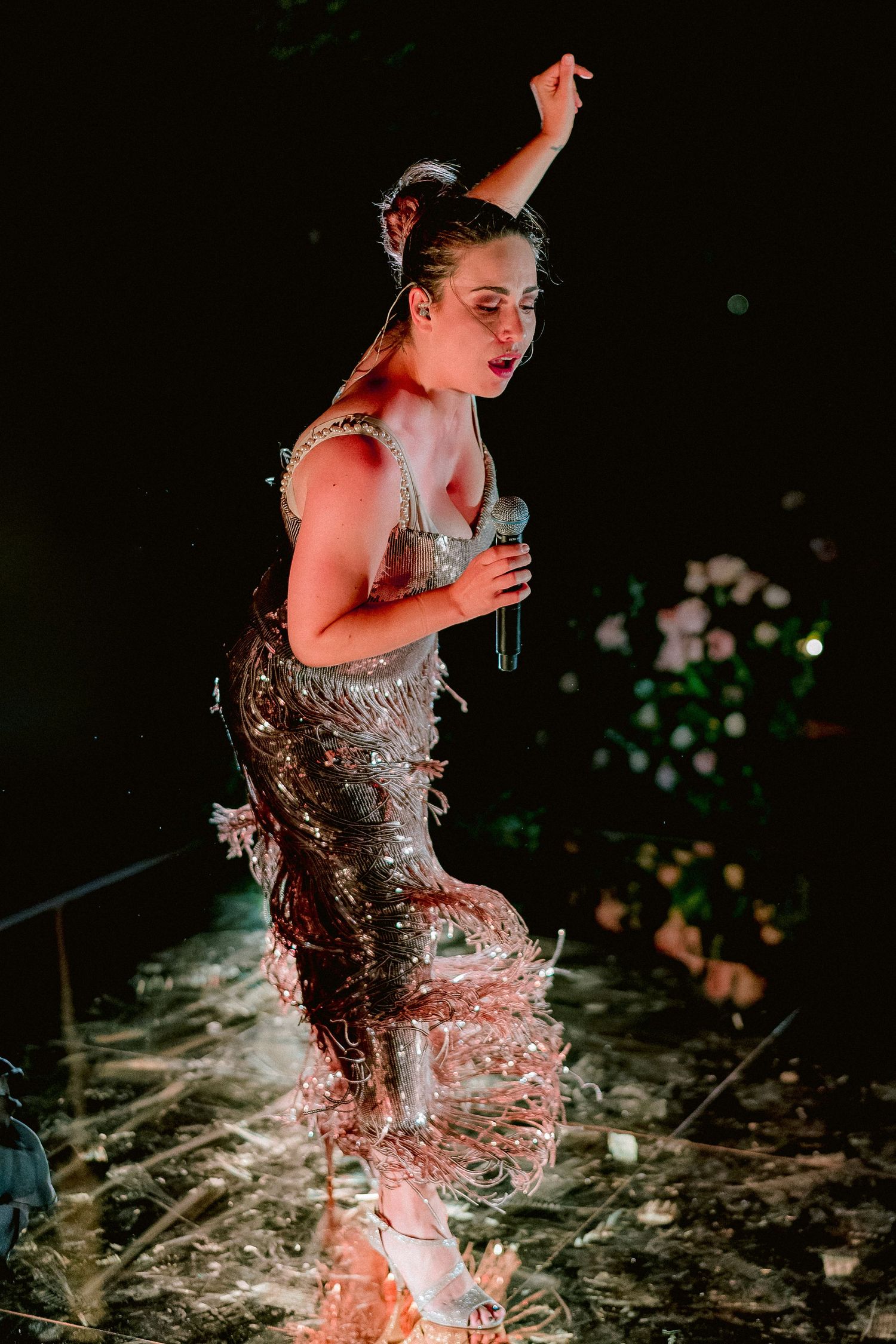 Performer in sparkling silver dress dances energetically on wet stage under dramatic lighting with splashing water effects.