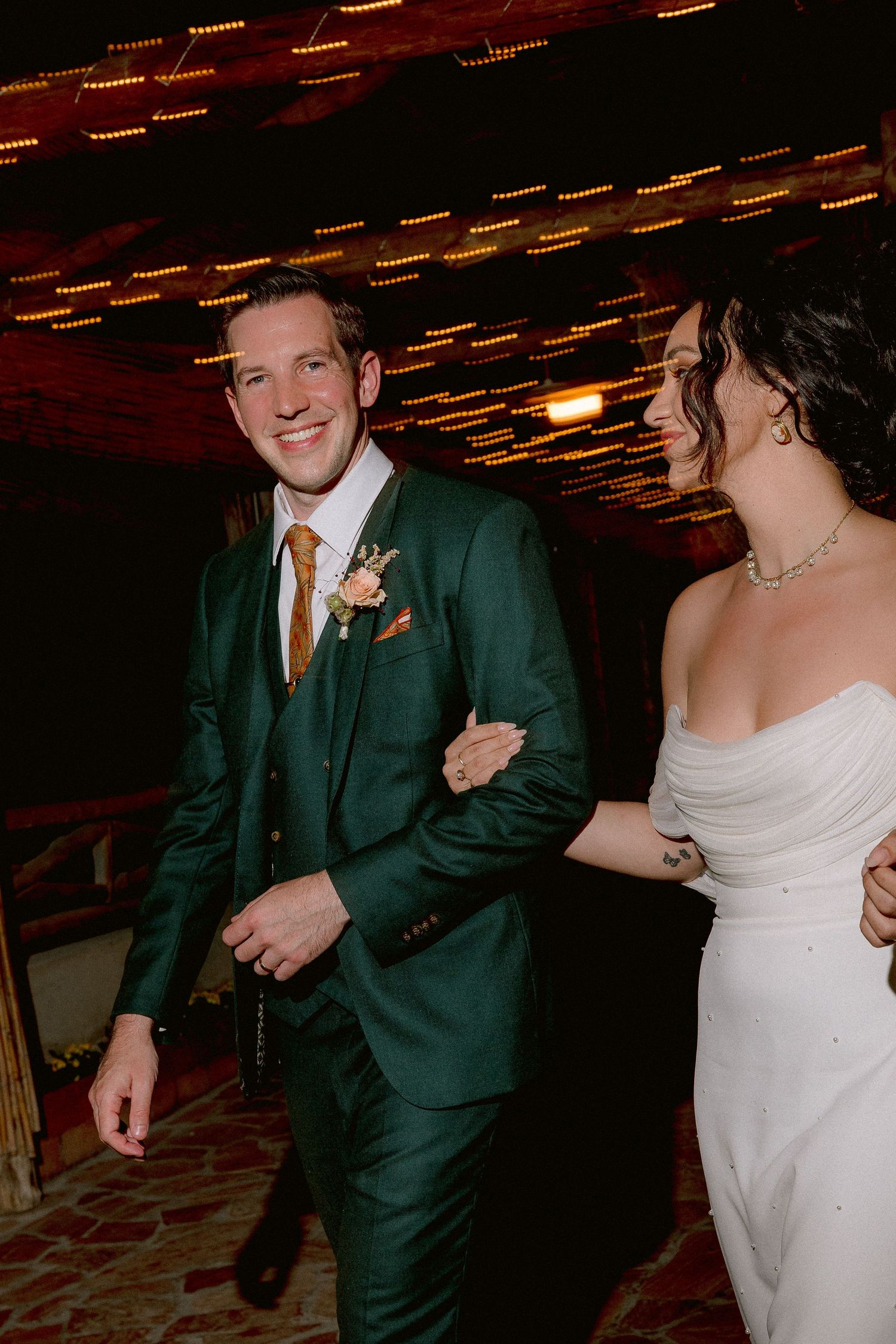 A couple celebrates at their wedding reception, with the groom wearing an elegant emerald green suit and the bride in white.