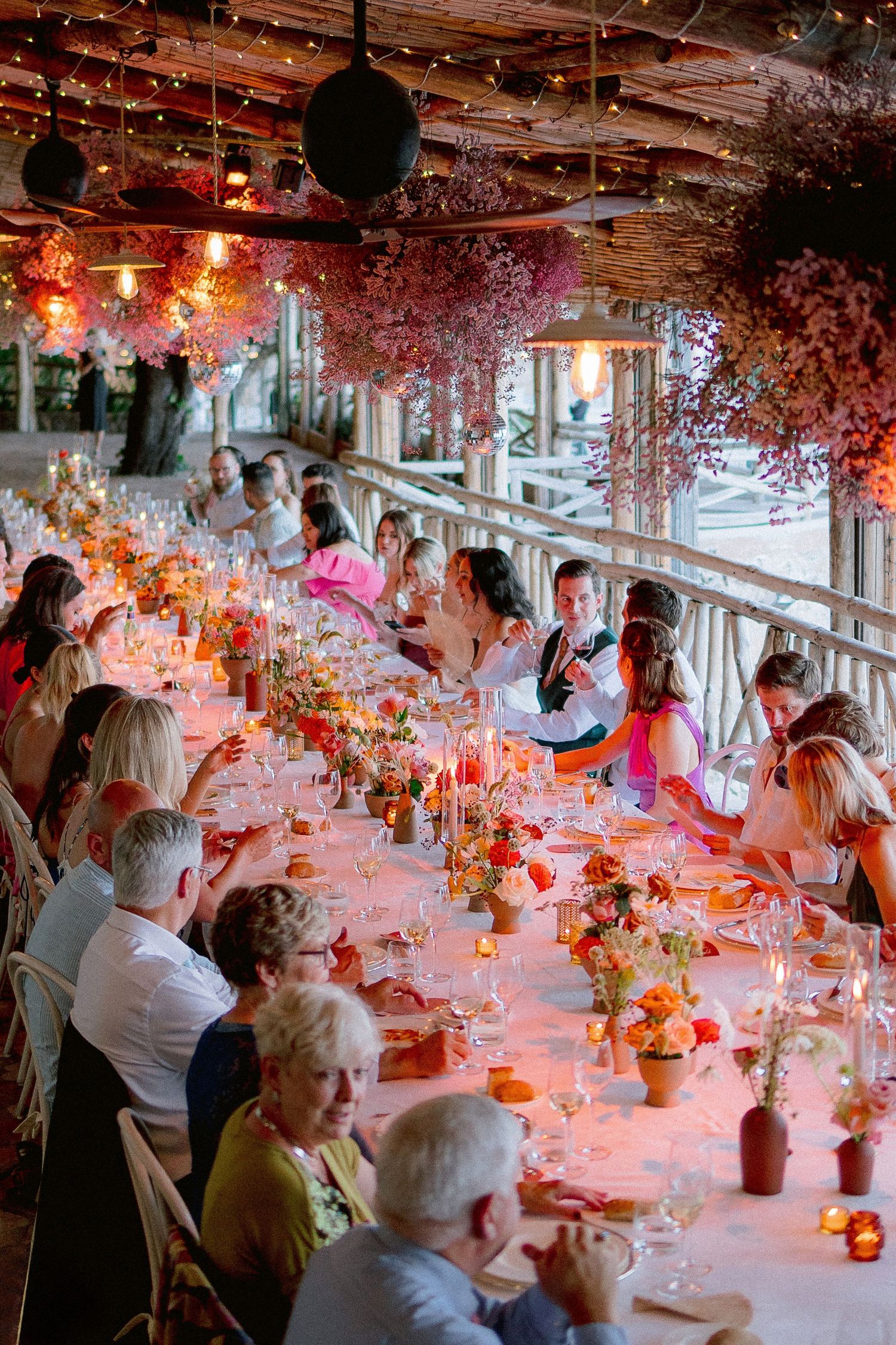 Elegant wedding reception dinner table with warm lighting, floral decorations, and guests seated in a romantic restaurant setting.