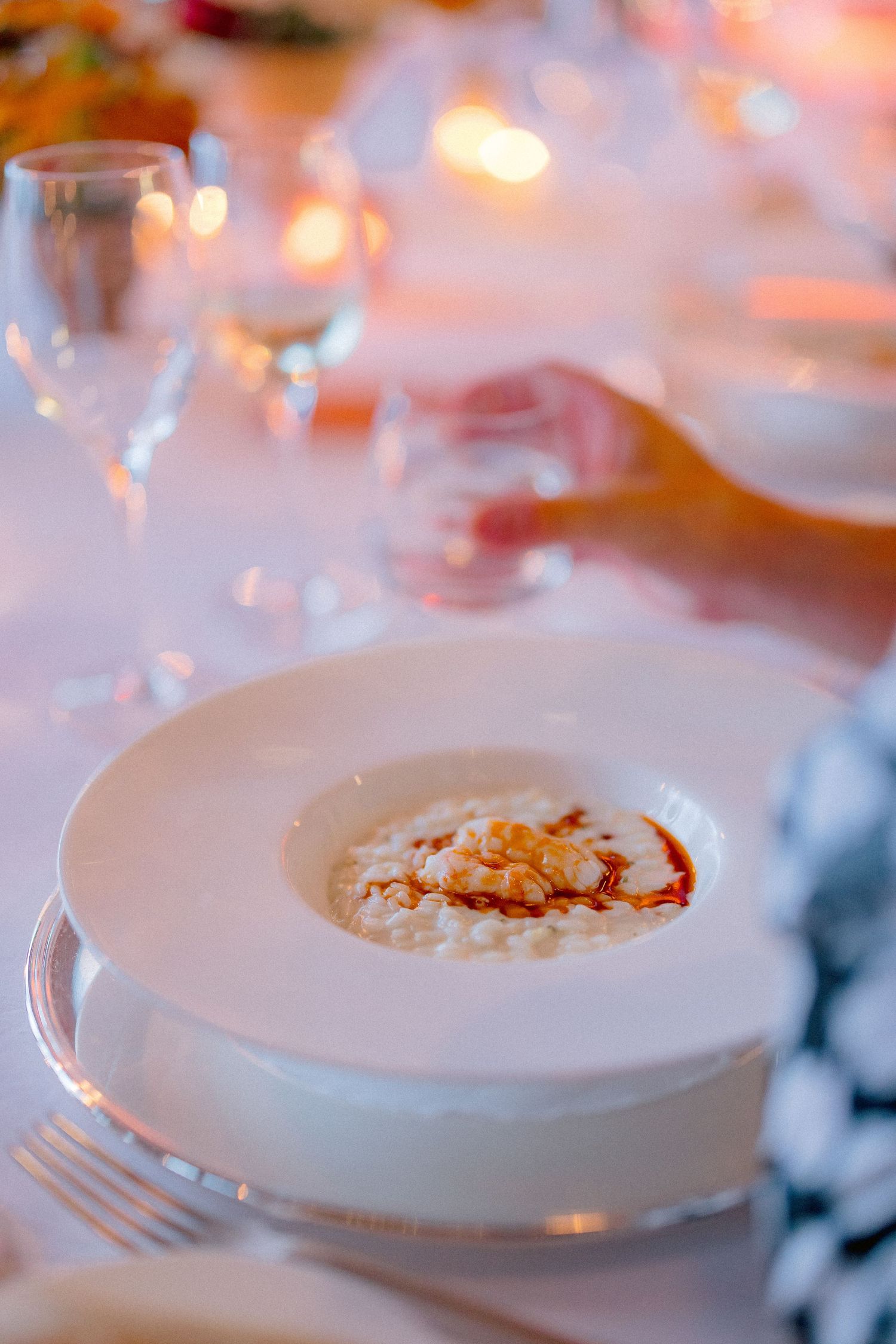 A creamy white soup garnished with red spices and toppings served in an elegant restaurant setting with soft lighting.