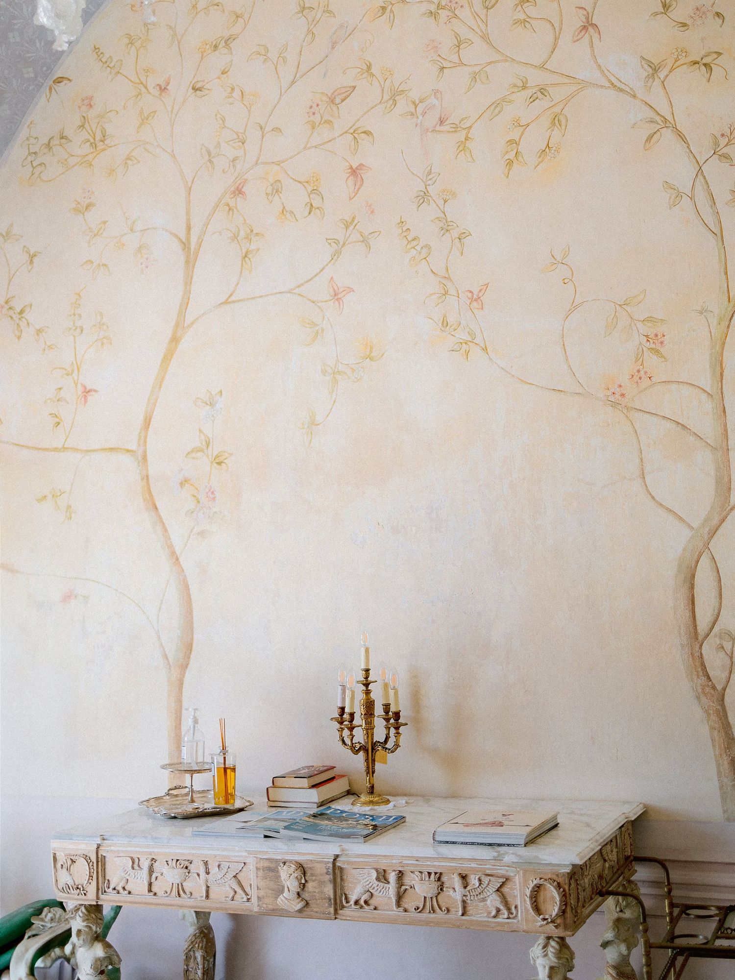 Elegant dining setup with candelabra on white table against wall with delicate gold leaf branch artwork.