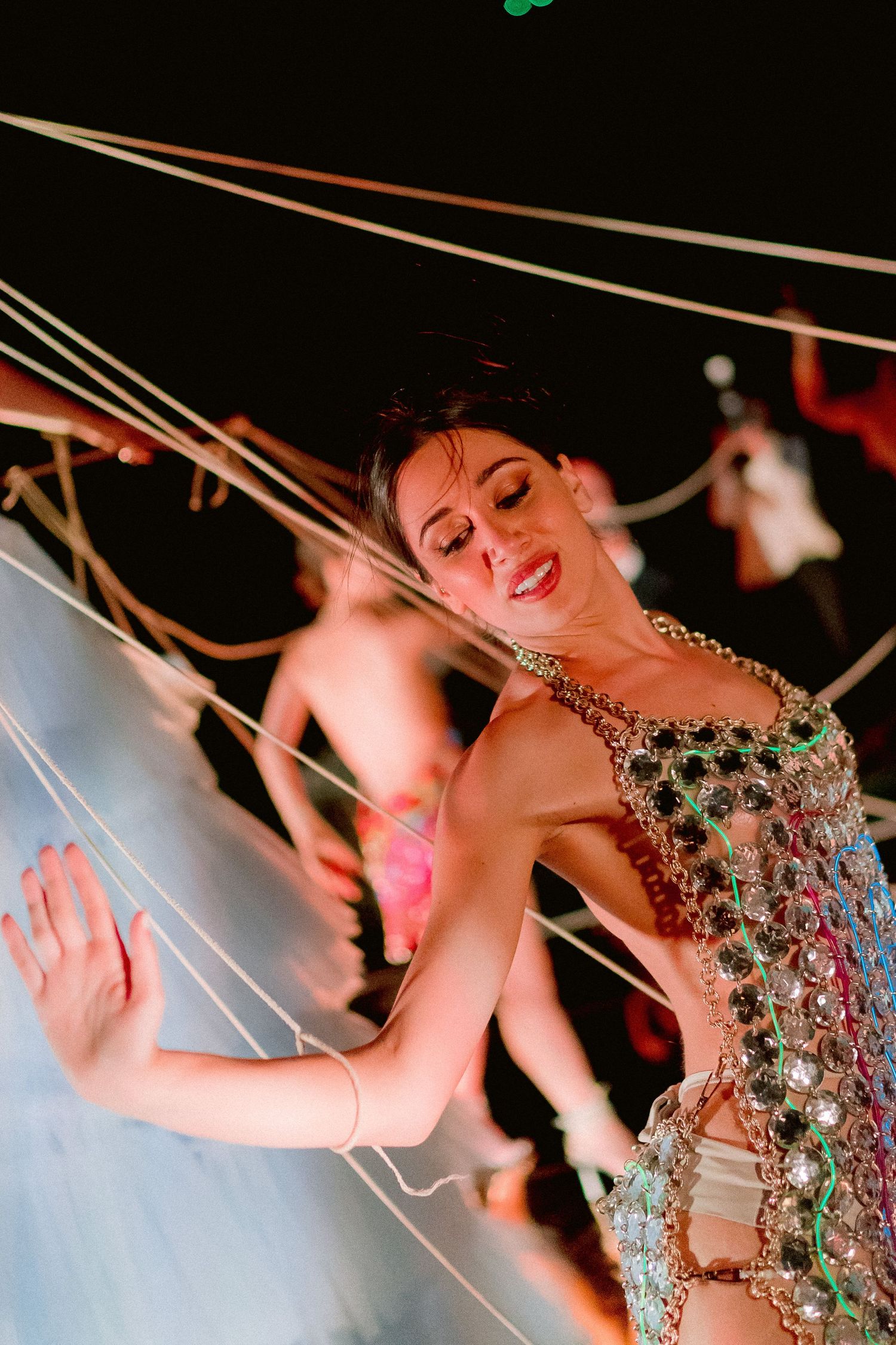 A performer in a sparkly jeweled costume smiles while dancing on stage during a theatrical performance.