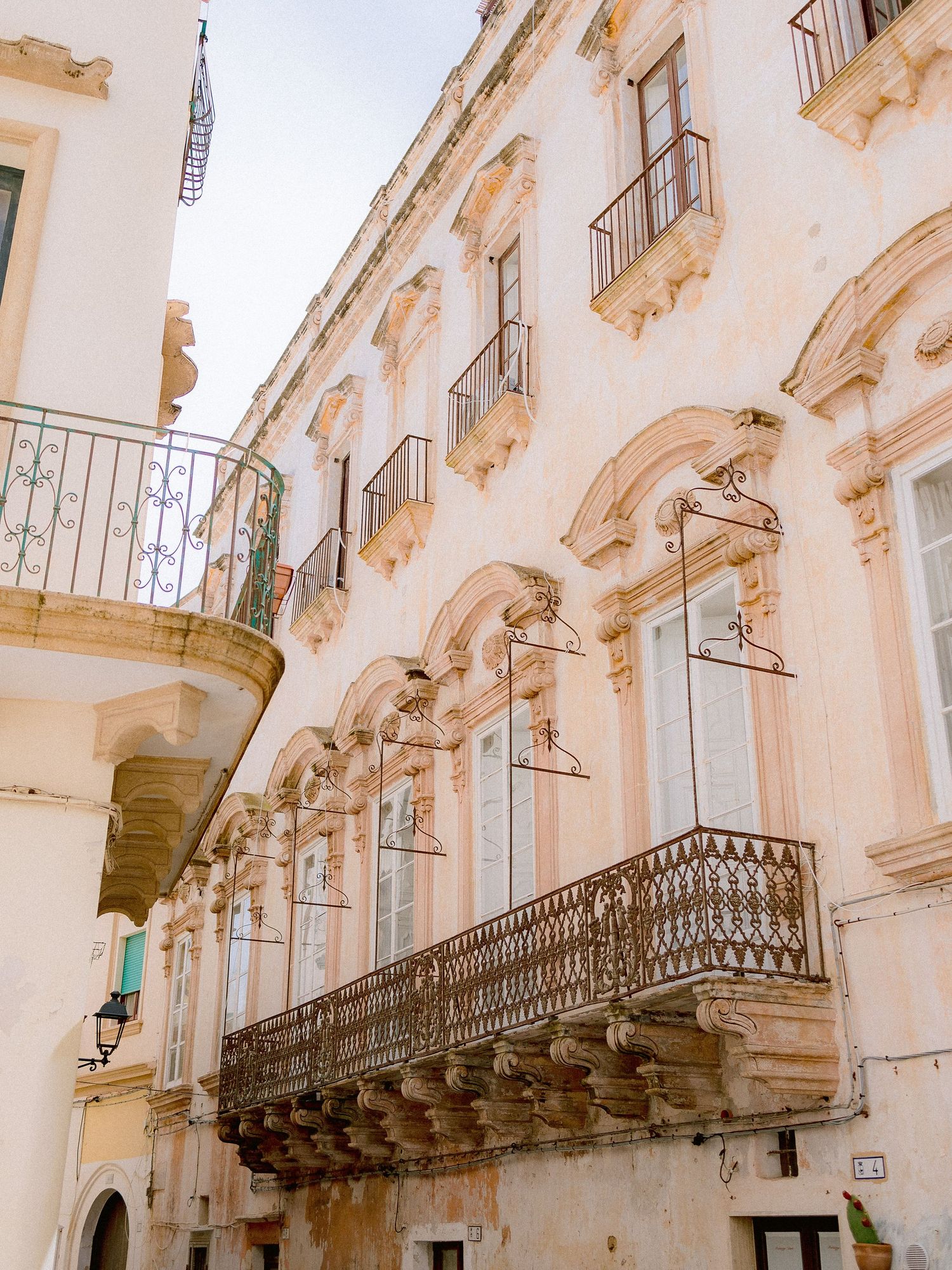 Historic white baroque building facade in Gallipoli, Puglia, with ornate balconies and decorative architectural details along windows.