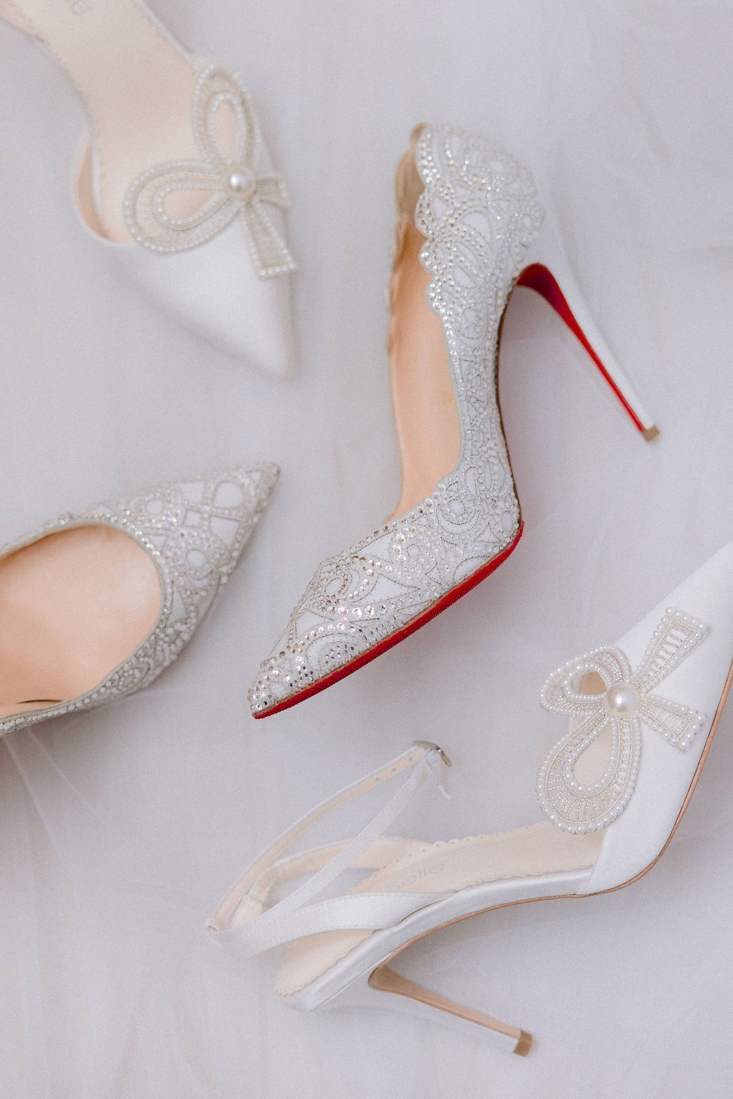 Elegant white lace bridal heels and slingback pumps with red soles arranged on light background.