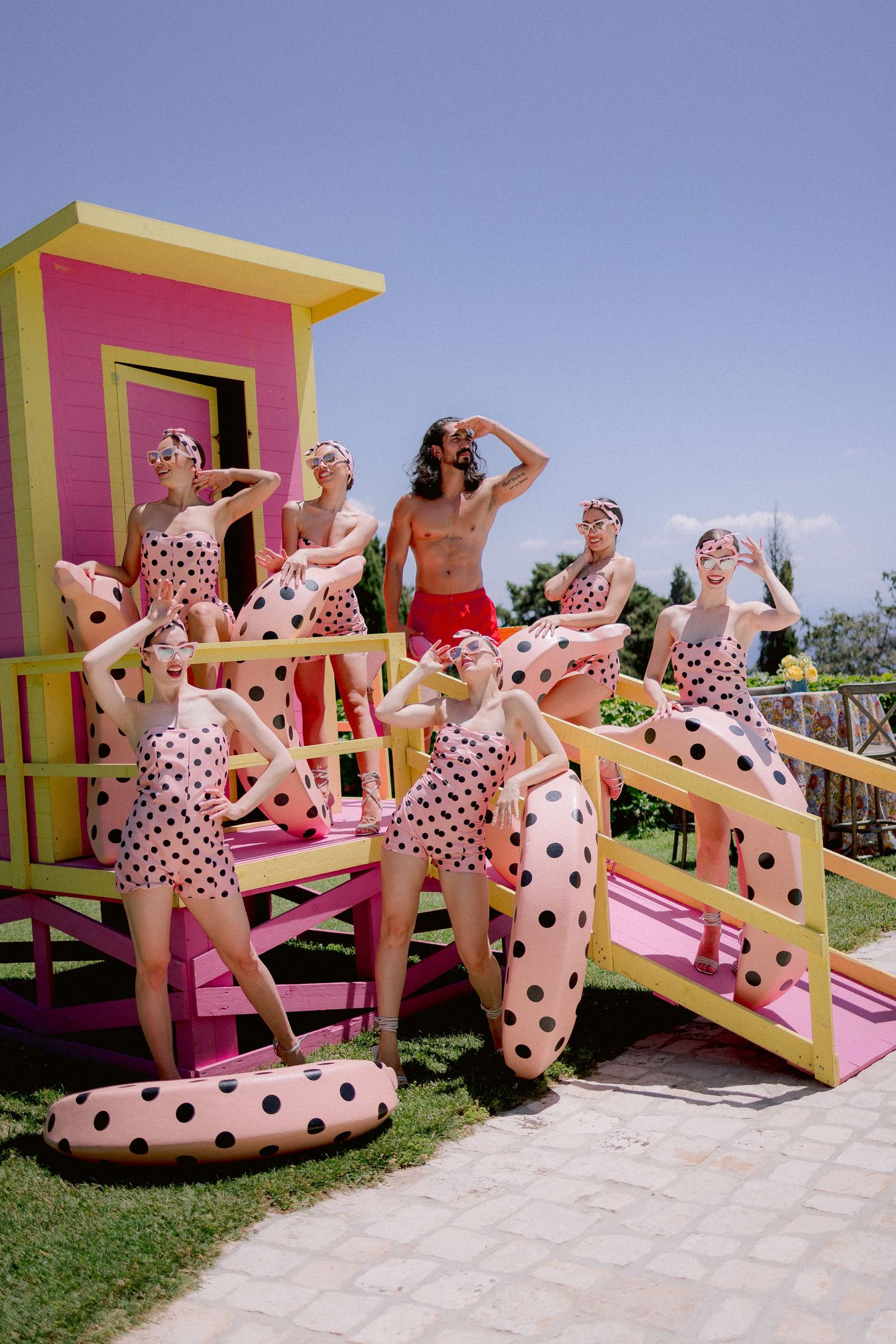 Retro summer scene with women in polka dot swimsuits posing on pink lifeguard tower at leisure park.