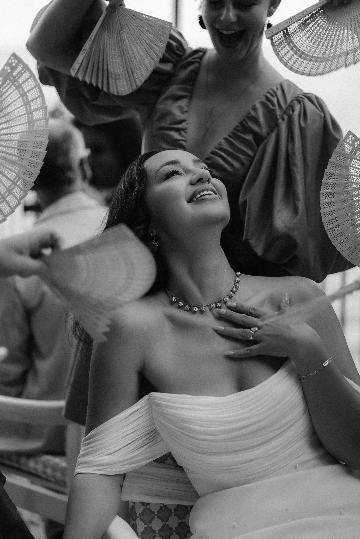 A black and white photo capturing a joyful moment with decorative folding fans surrounding a person in an off-shoulder dress.