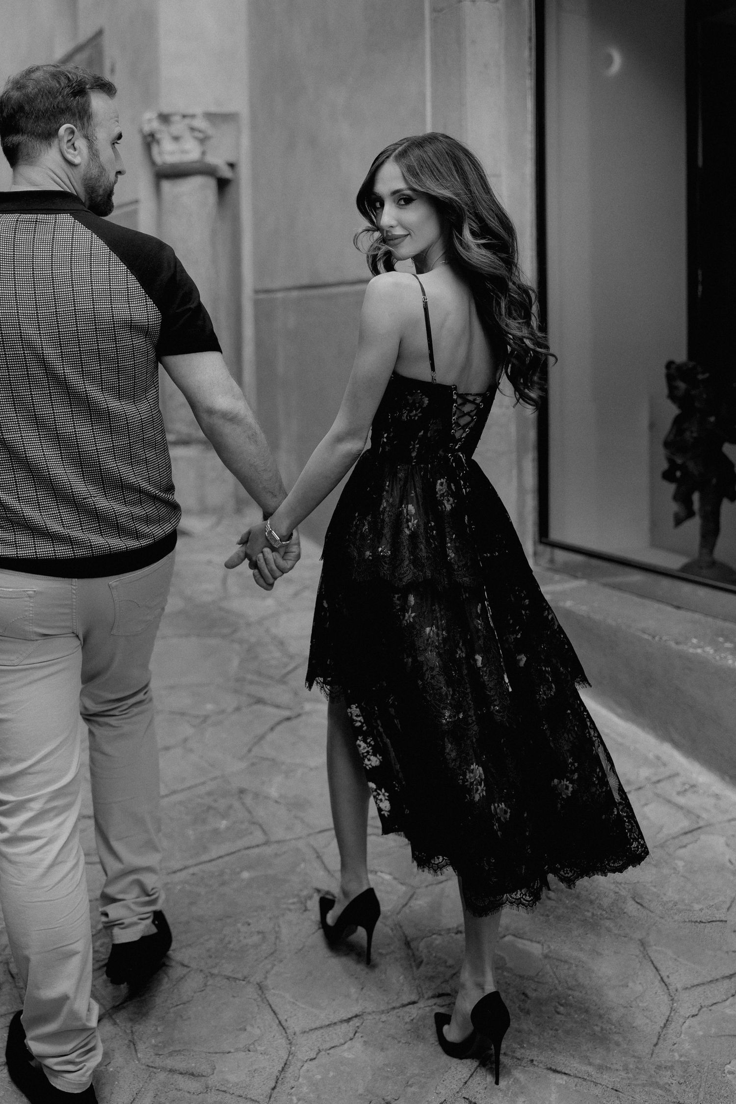 A romantic black and white photo of a couple holding hands, with a woman in an elegant black lace dress walking together.
