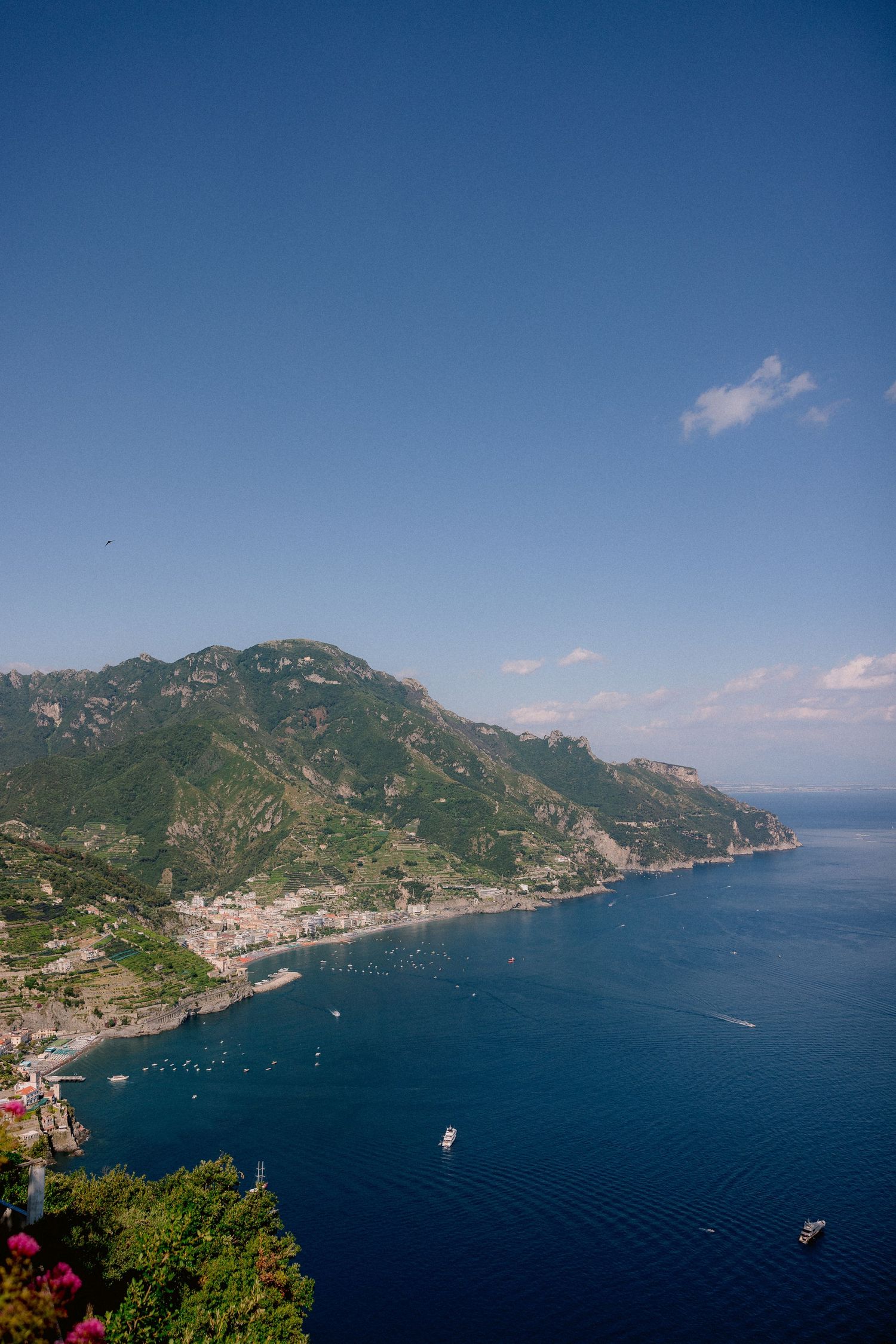 Aerial view of the Amalfi Coast in Italy showing dramatic cliffs, blue Mediterranean waters, and small boats in the bay.