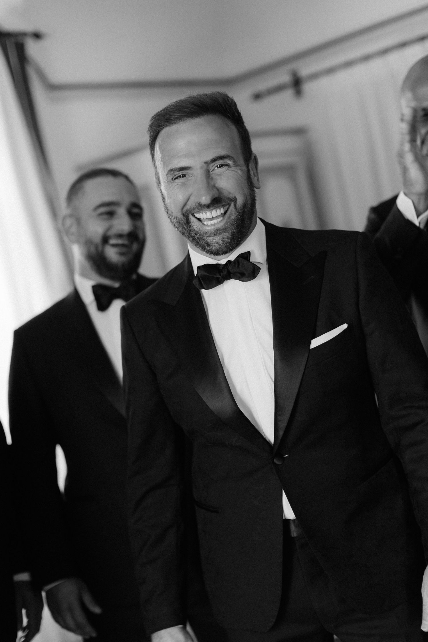 Guests in black tie attire share a genuine laugh at an elegant formal event.