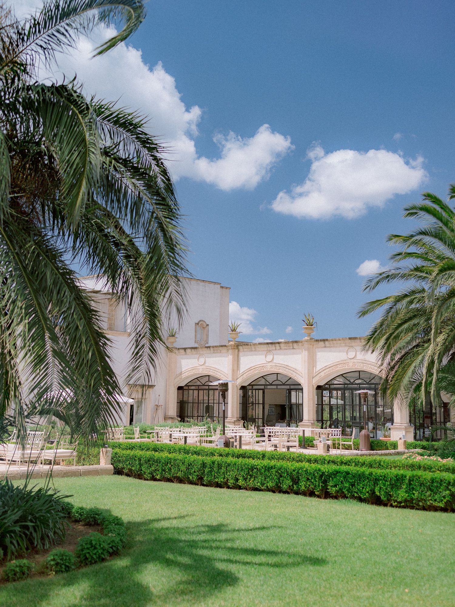 Mediterranean architectural villa with arched windows and palm trees framing a manicured lawn under blue skies.