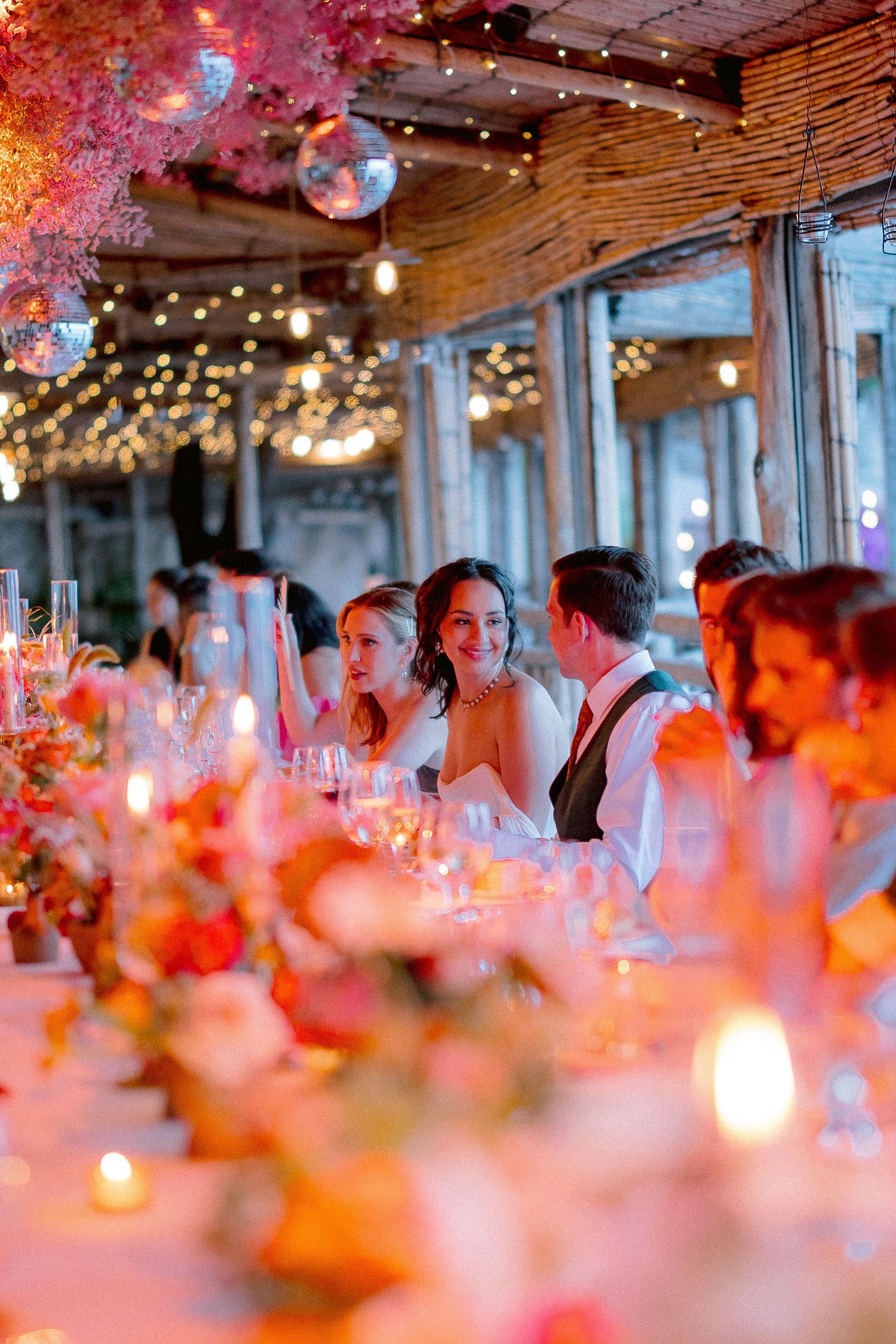Wedding reception venue decorated with string lights and pink flowers as guests enjoy an intimate dinner celebration.