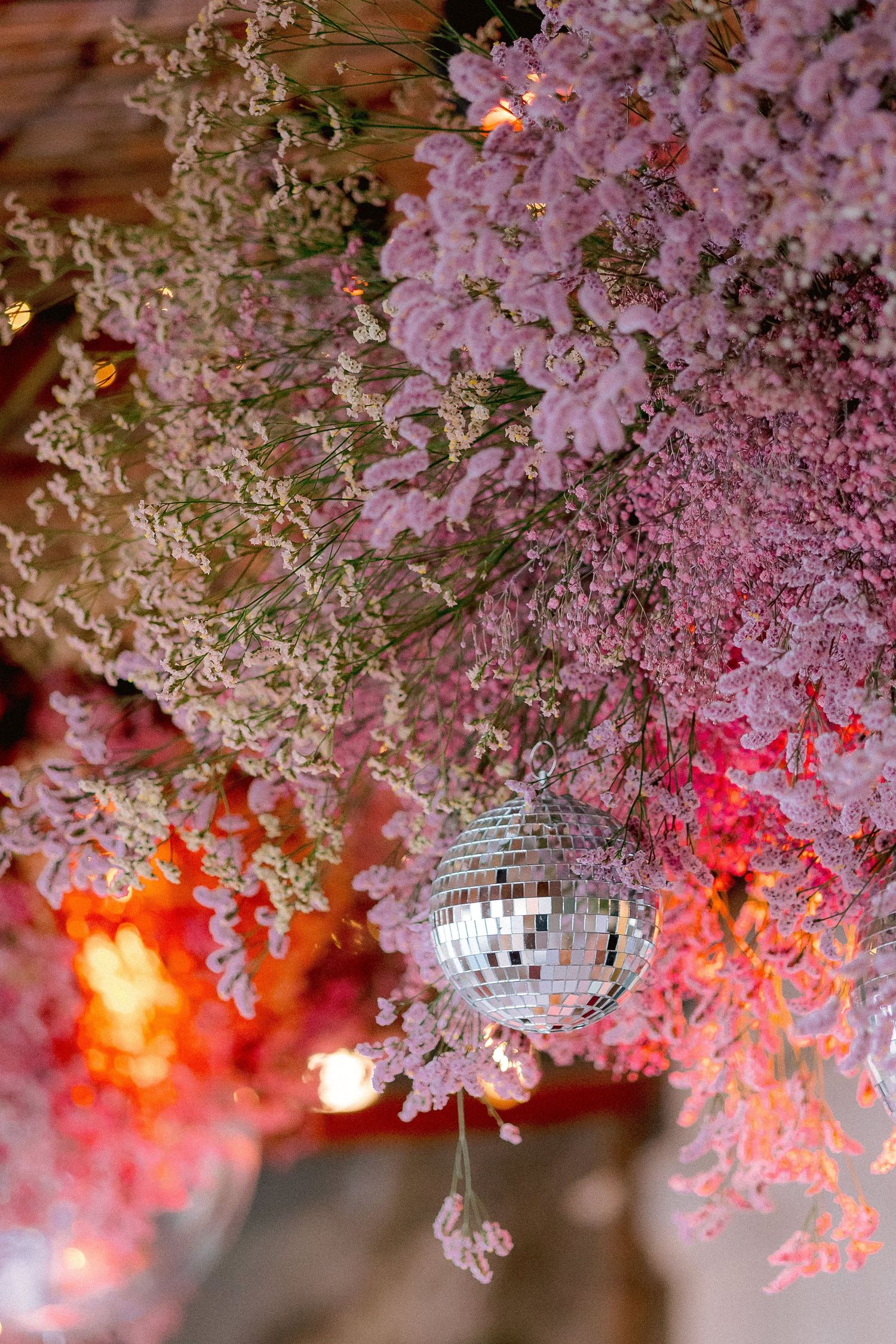 Disco ball hanging among pink cherry blossoms with red lighting creating a dreamy party atmosphere.