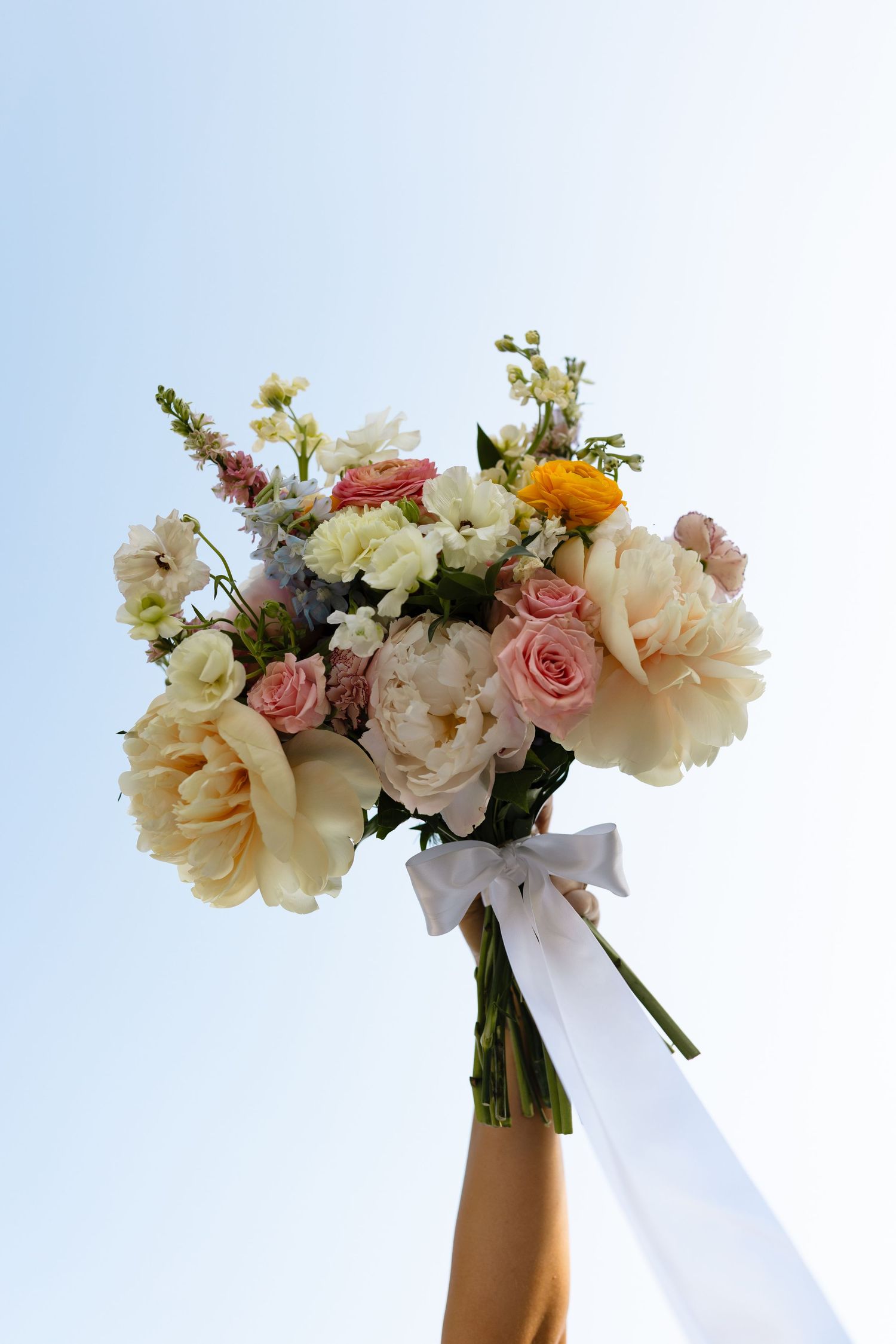 Three elegant bridal bouquets with pink and white roses, peonies and other blooms tied with white ribbons against a light background.