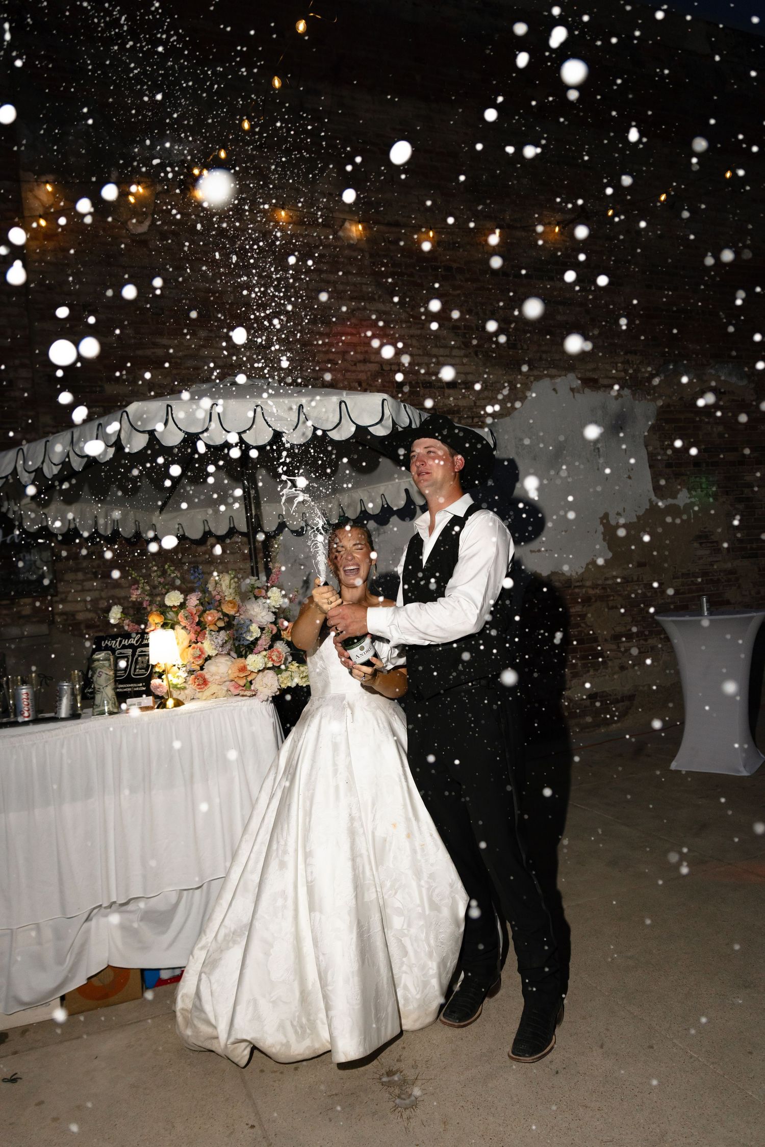 A couple shares their first dance at a snowy winter wedding reception with snowflakes falling around them in the evening.