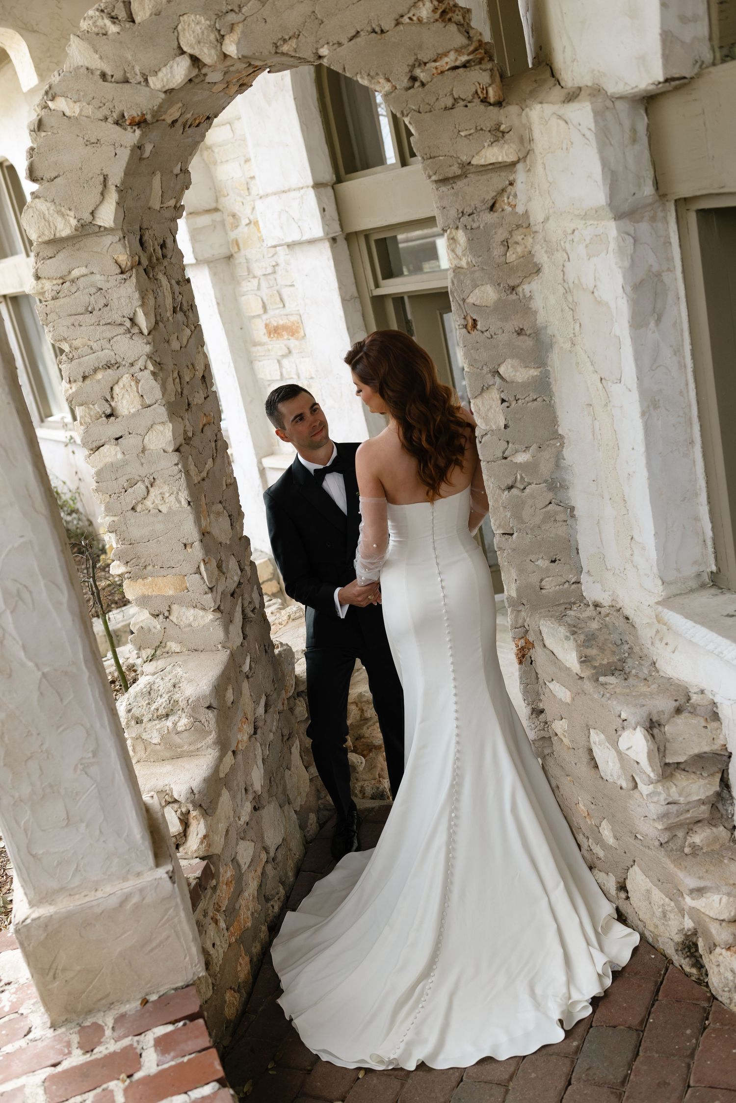A romantic wedding photography series shows couple embracing in a rustic stone corridor with natural lighting.