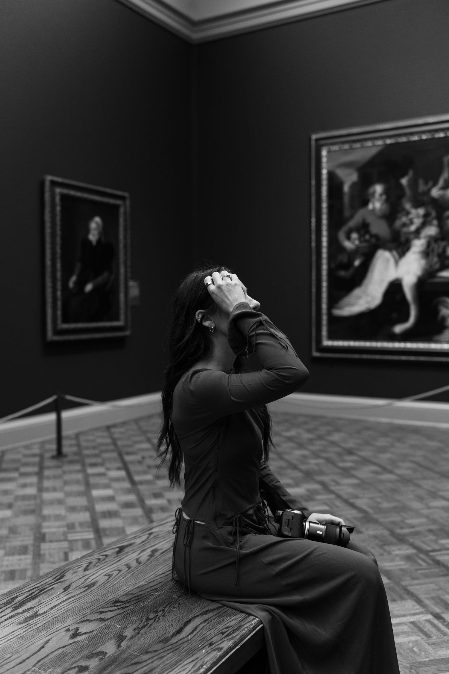 A series of black and white photos showing someone lying down and looking at artwork in a darkened gallery space.