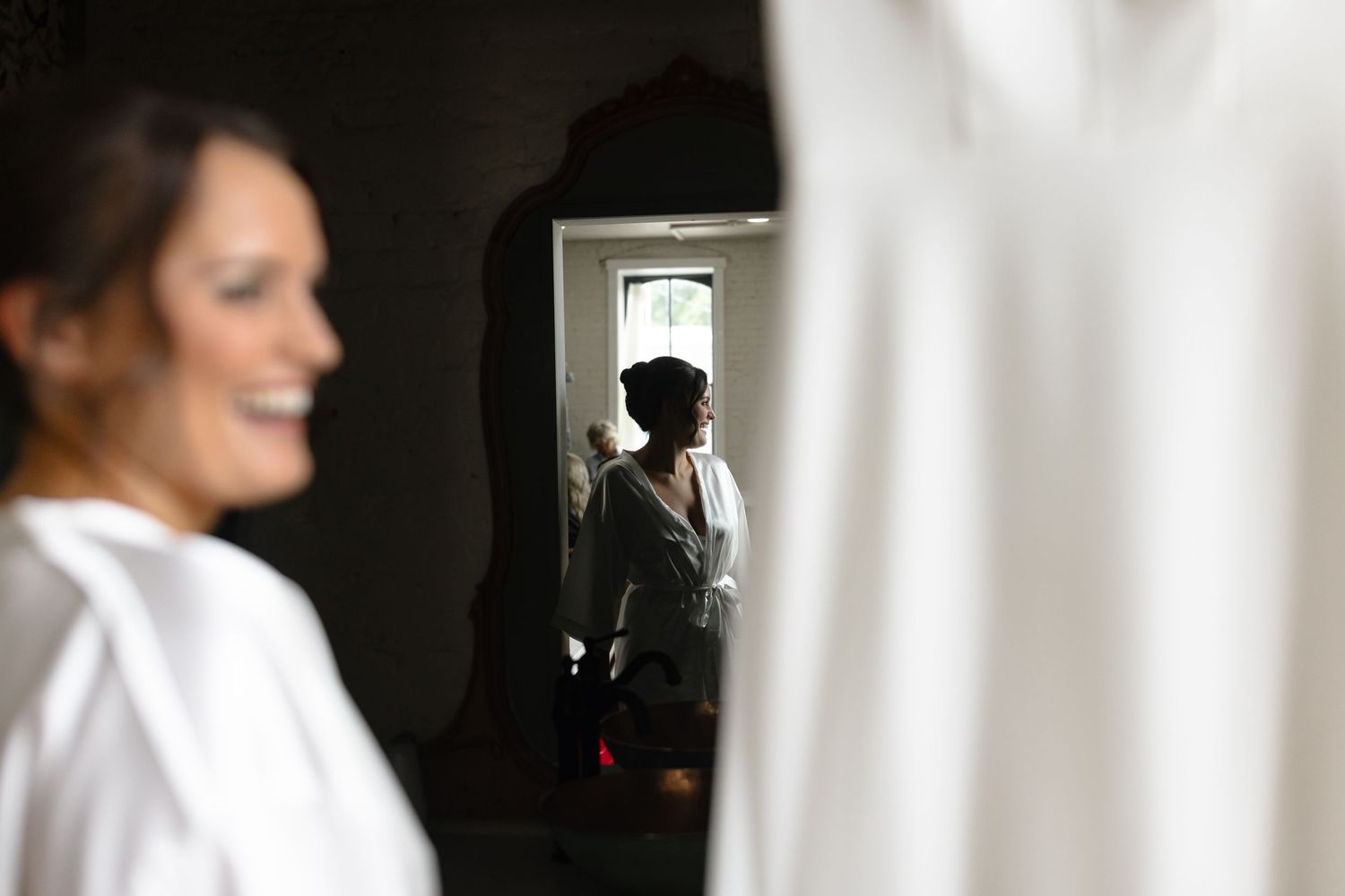 A silhouetted figure reflected in a mirror while someone in a white shirt stands blurred in the foreground.