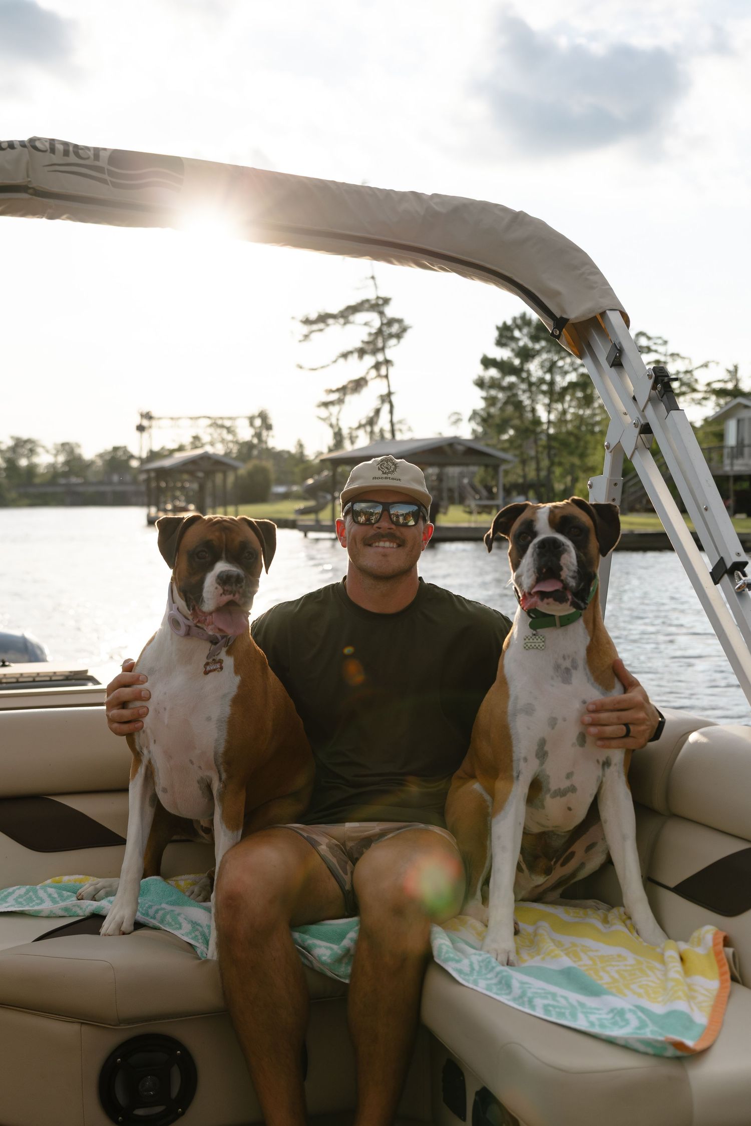 Two boxer dogs sitting on a boat with their companion enjoying a sunny day on the water.