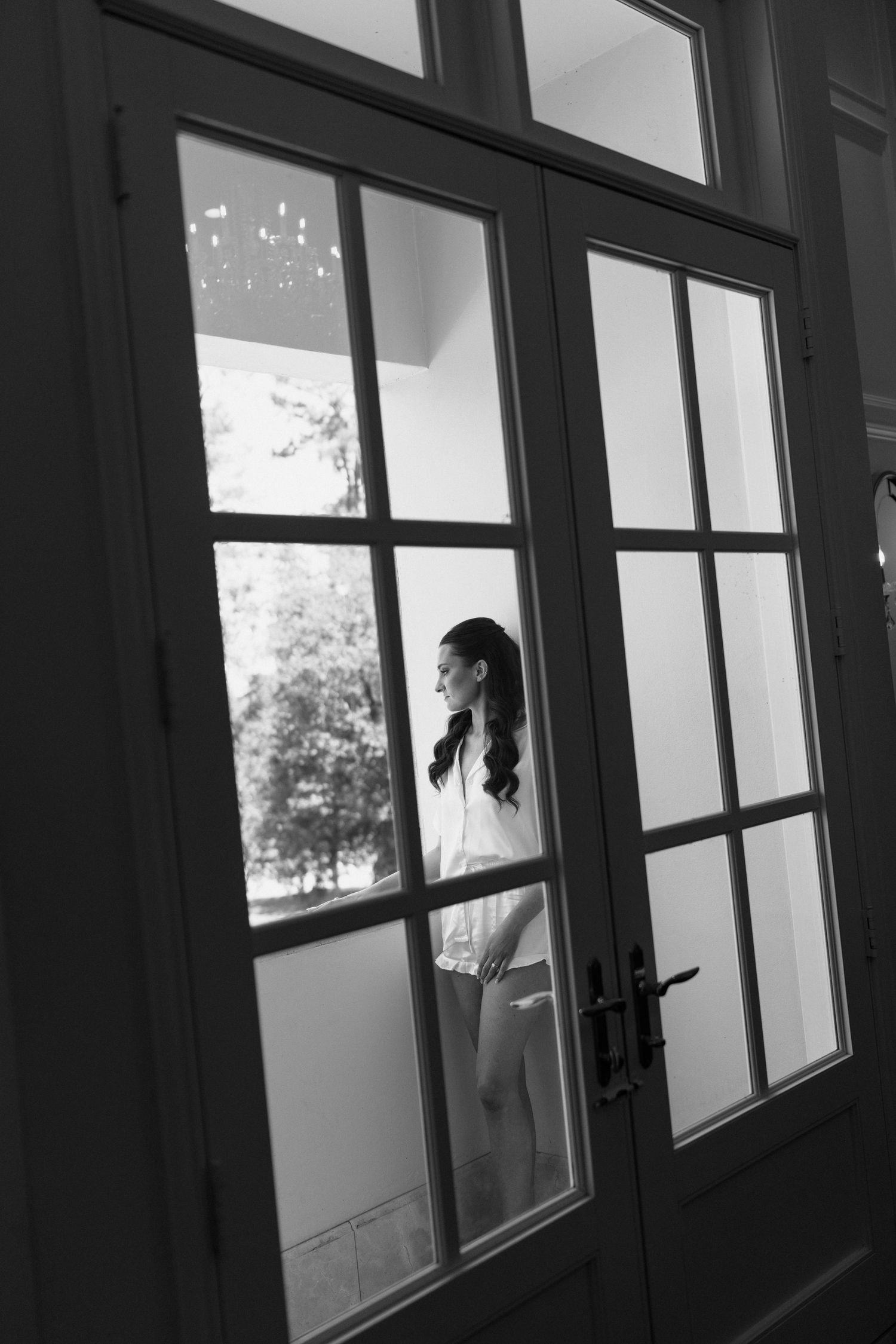 Black and white interior hallway with large windows casting shadows and creating a moody architectural perspective.
