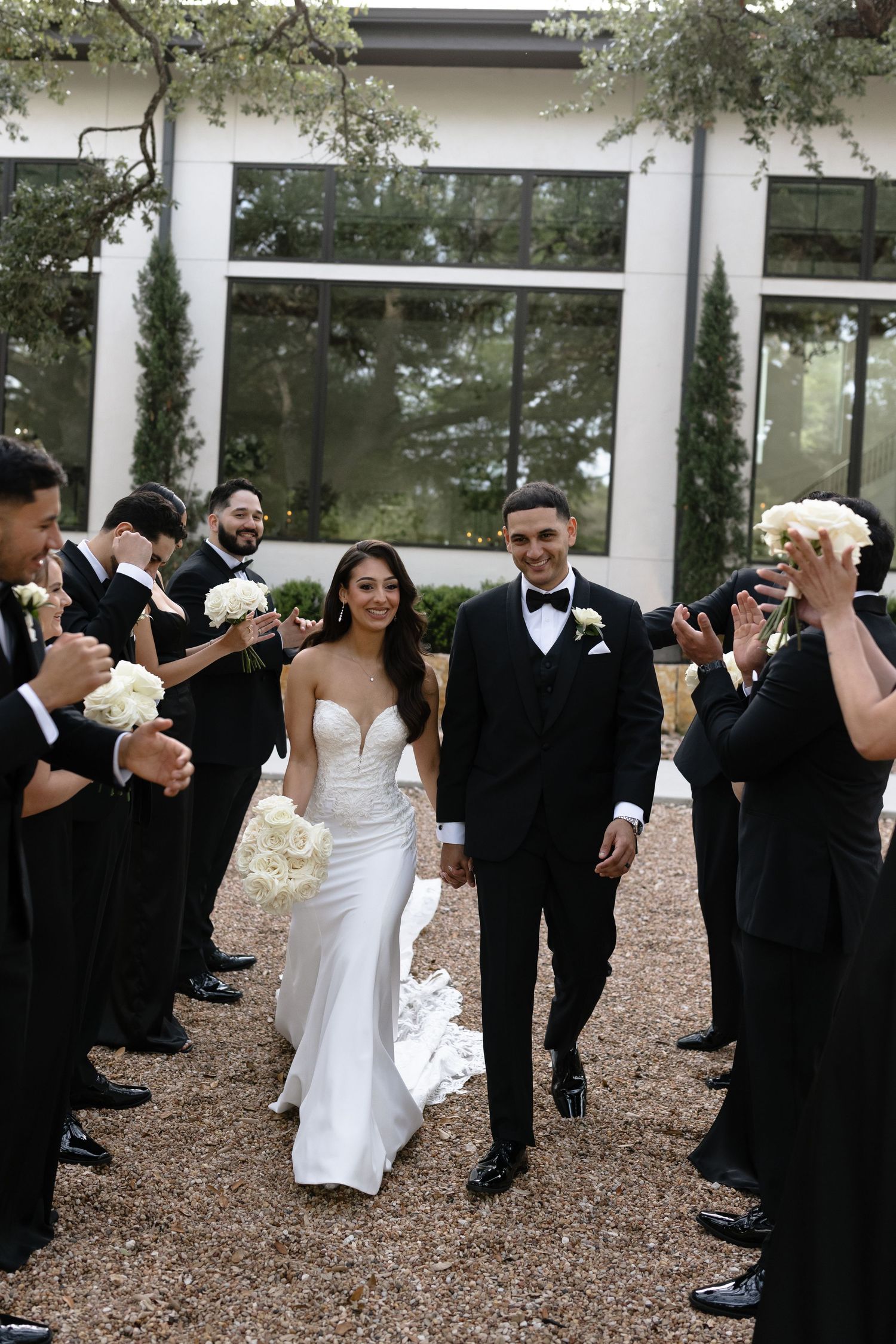 Wedding party wearing black and white formal attire dance together in a courtyard during celebration.