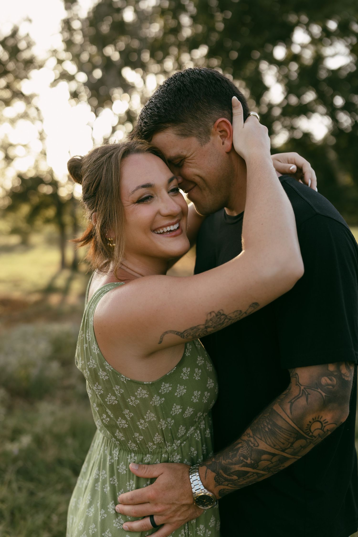 A couple shares intimate moments in nature wearing a green floral dress and dark clothing during golden hour photography.