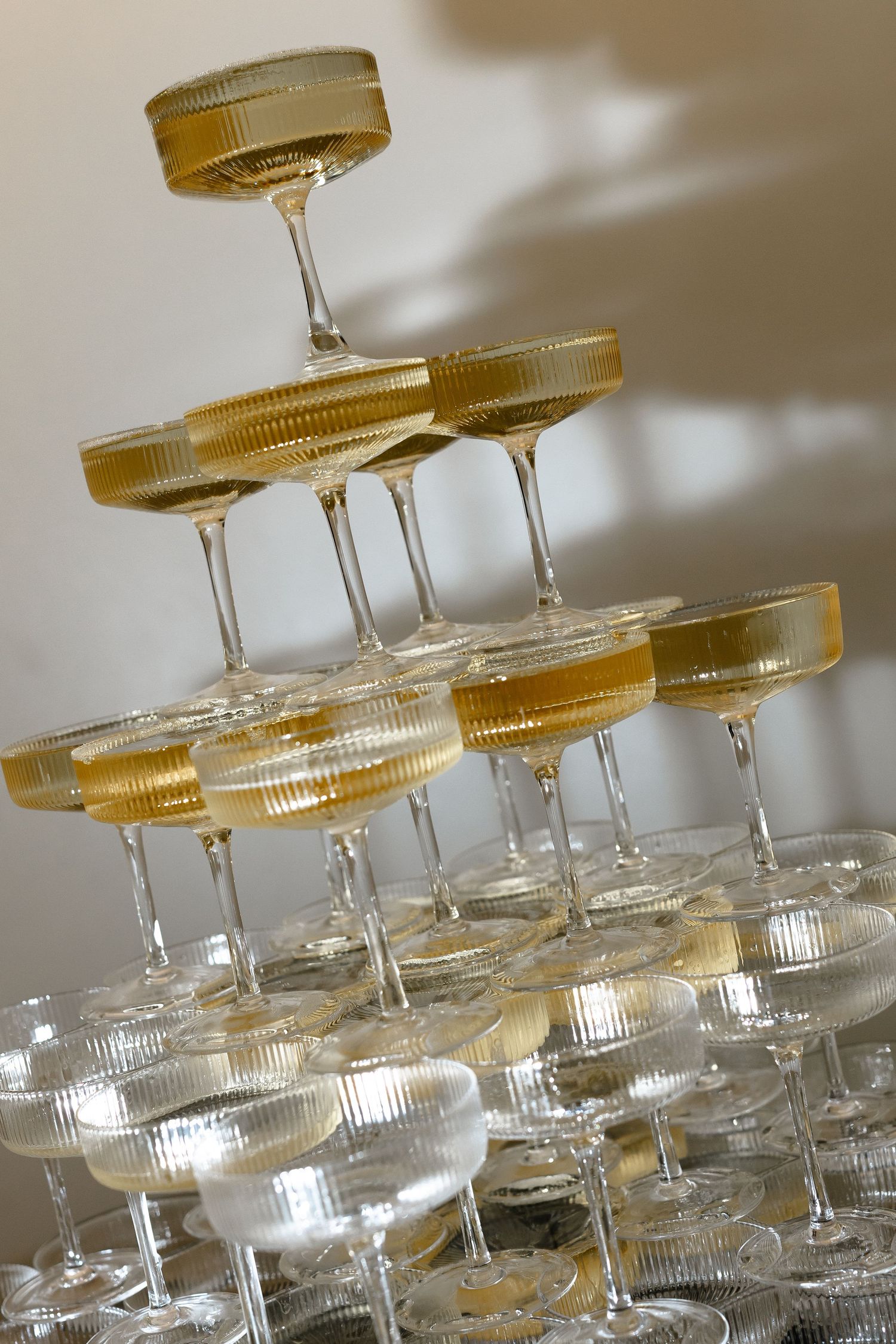 A close-up view of stacked glass champagne coupe glasses arranged in a tiered tower formation with a golden glow.