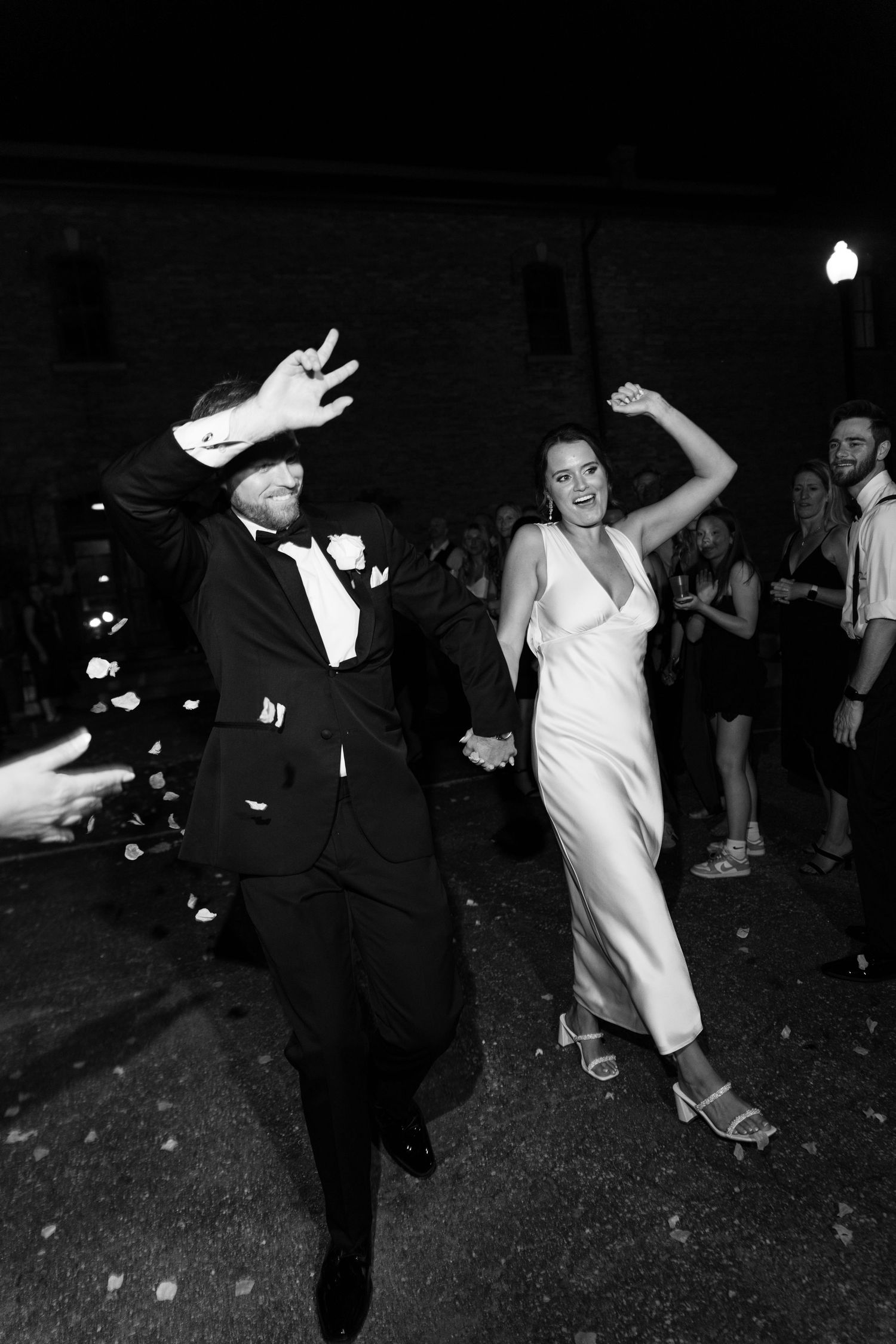A couple dances joyfully at a formal event, with the man in a tuxedo and woman in a sleek white dress.