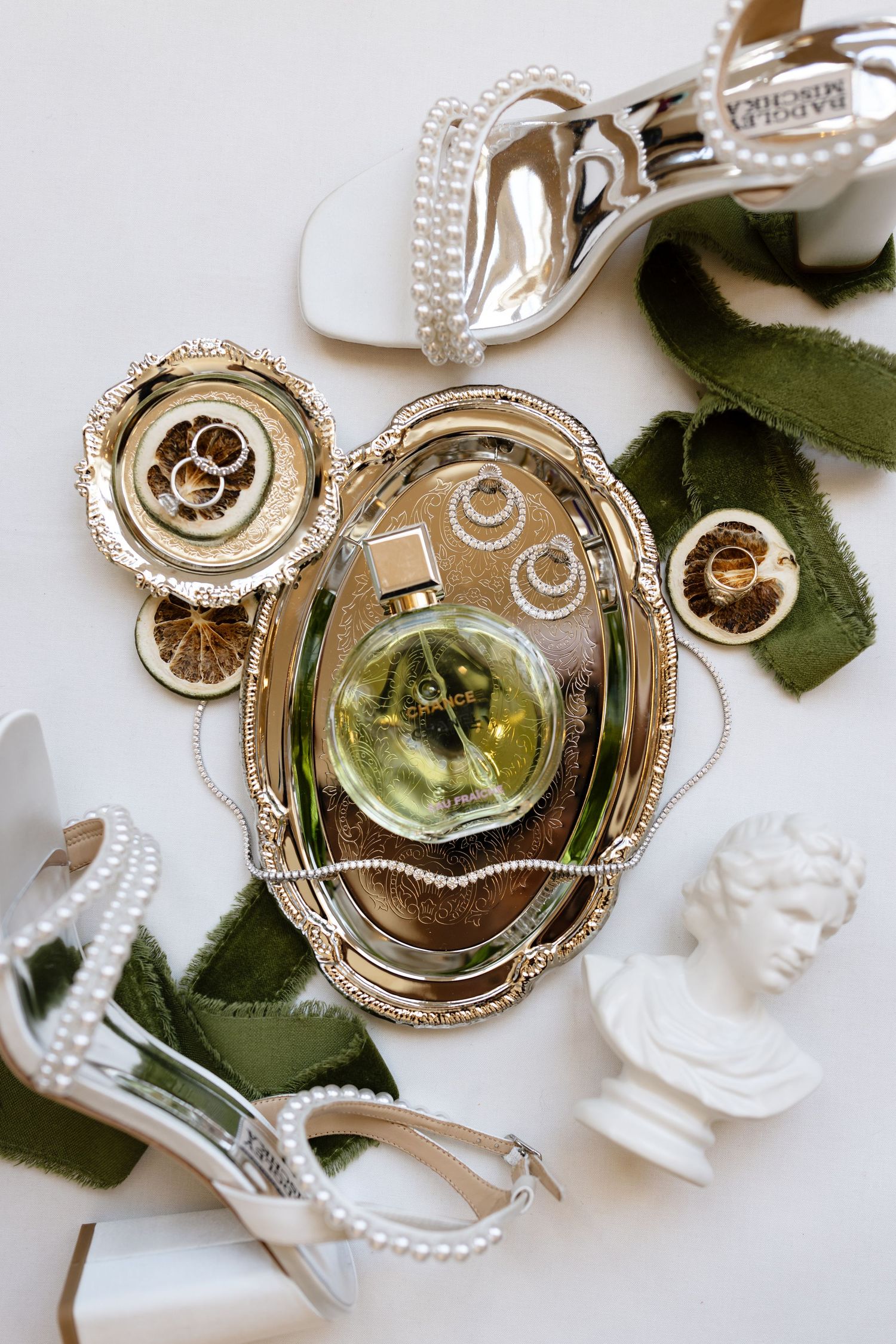 Artistic jewelry flatlay showcasing vintage-style gold lockets with green fabric leaves and white decorative elements on white surface.