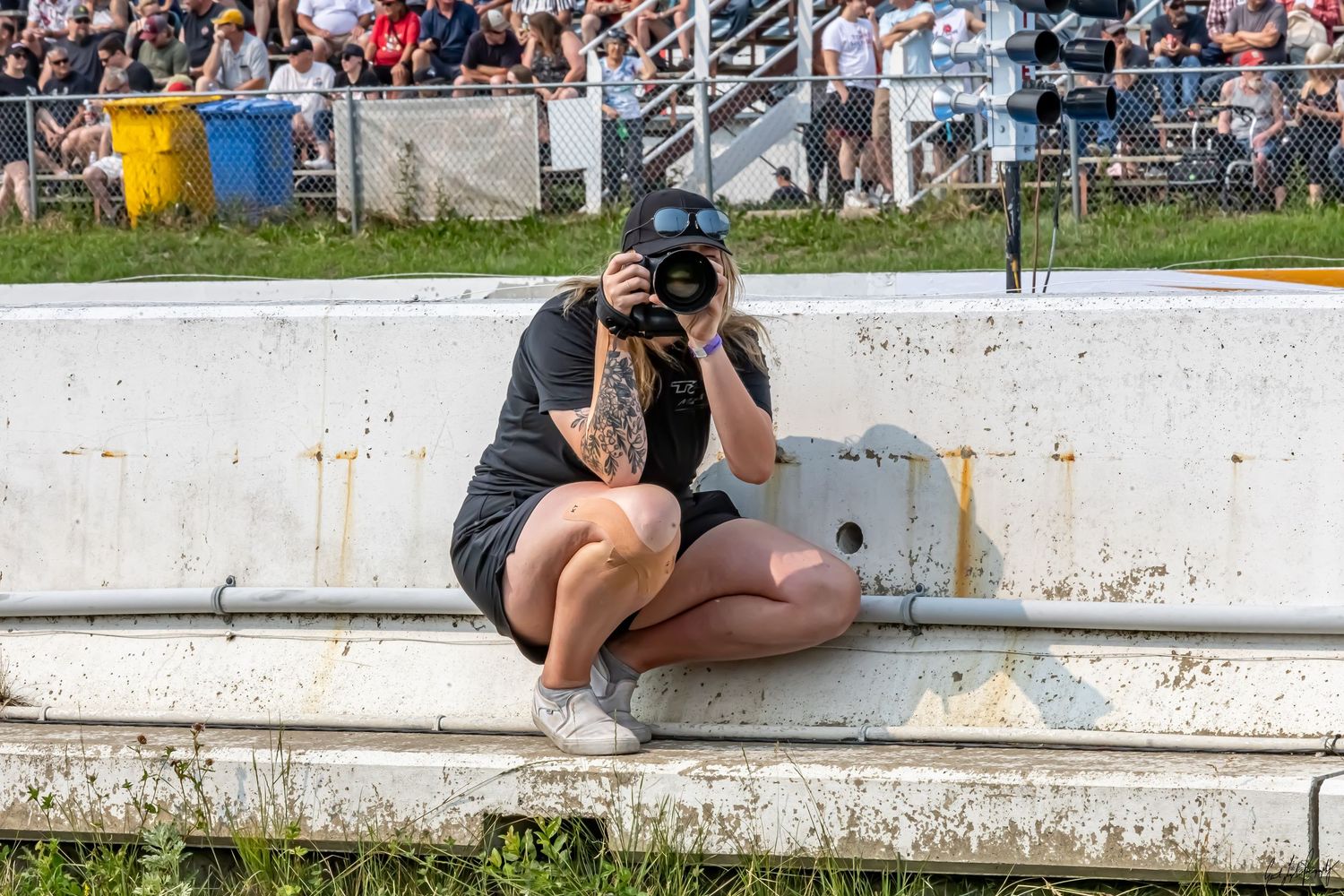 Becky crouched on pit wall with a camera mid-shot, repping Fuelled Up Photography at the track.