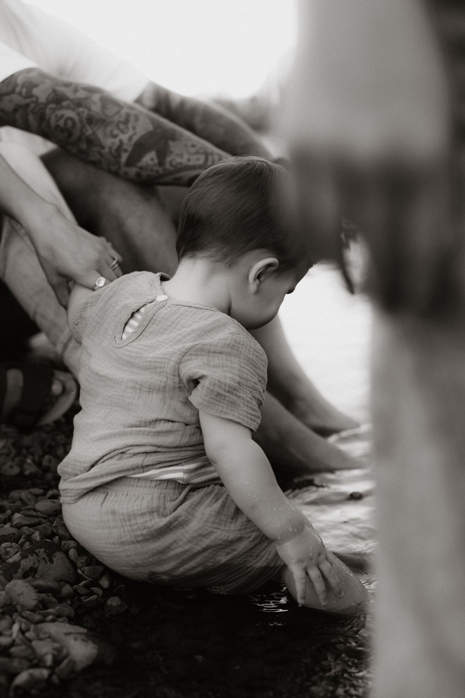 Black and white photo of a small child in light colored clothing playing near water.