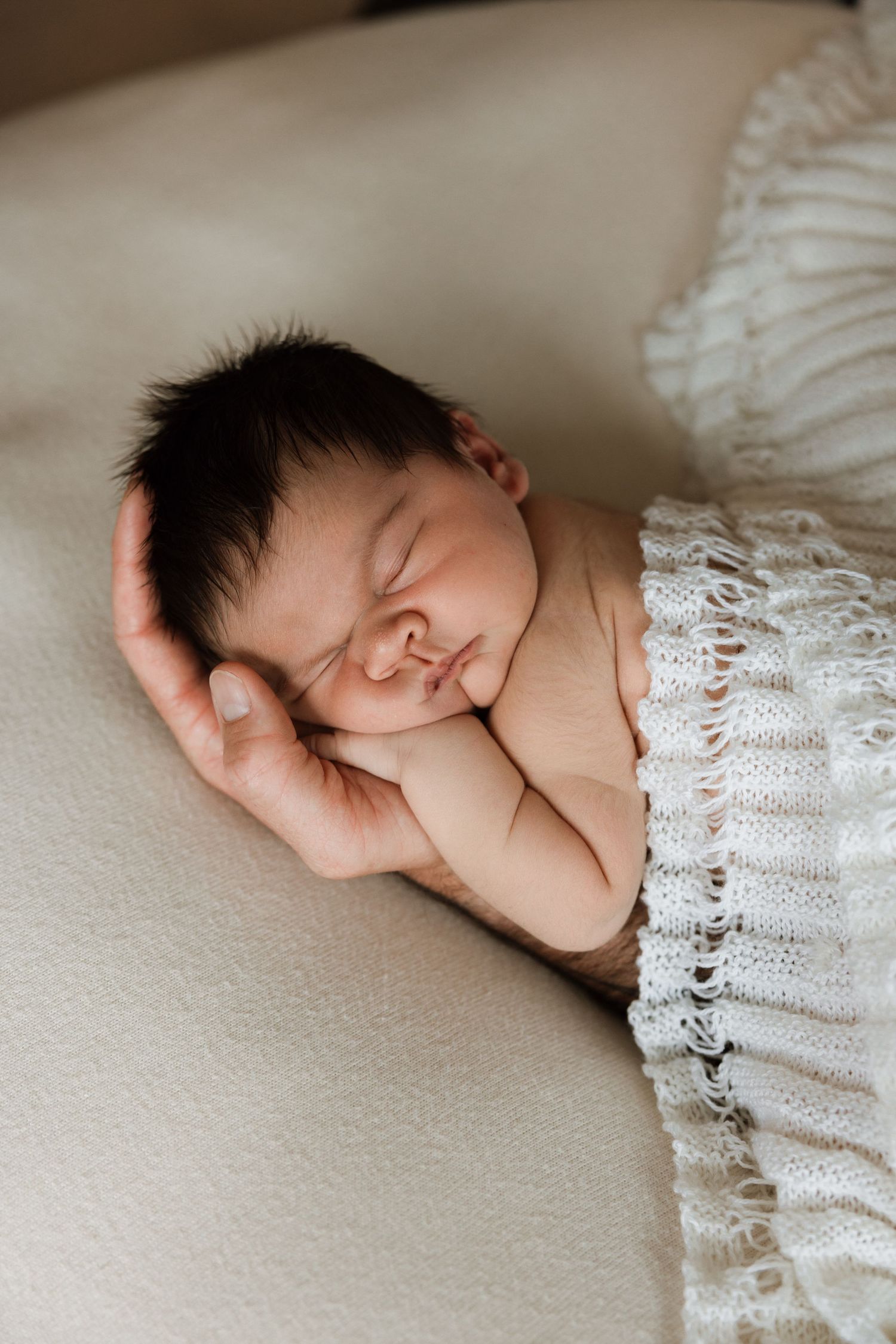 Delicate newborn photography featuring baby sleeping against lace and neutral fabric.