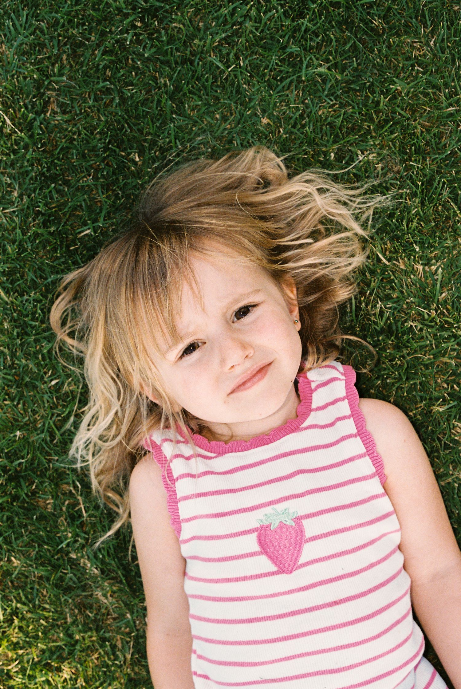 Young child lying on grass wearing a pink and white striped tank top with heart design.