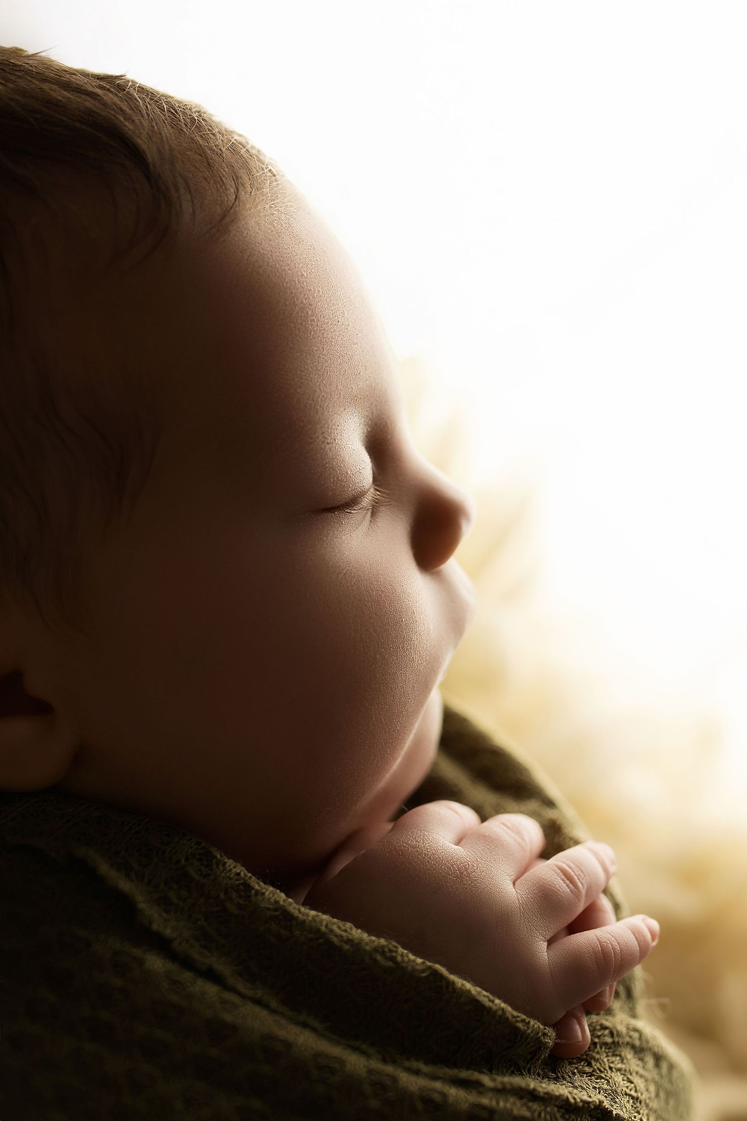 A sleeping infant rests peacefully on a soft green blanket in warm lighting.