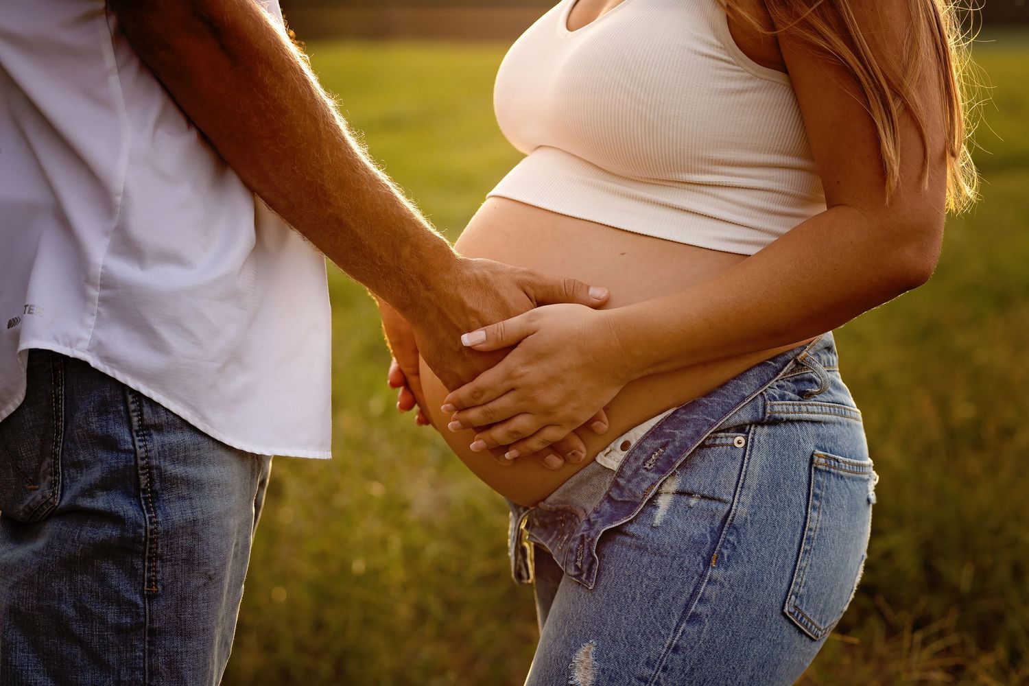 Close-up of expecting couple's hands tenderly cradling baby bump at sunset.