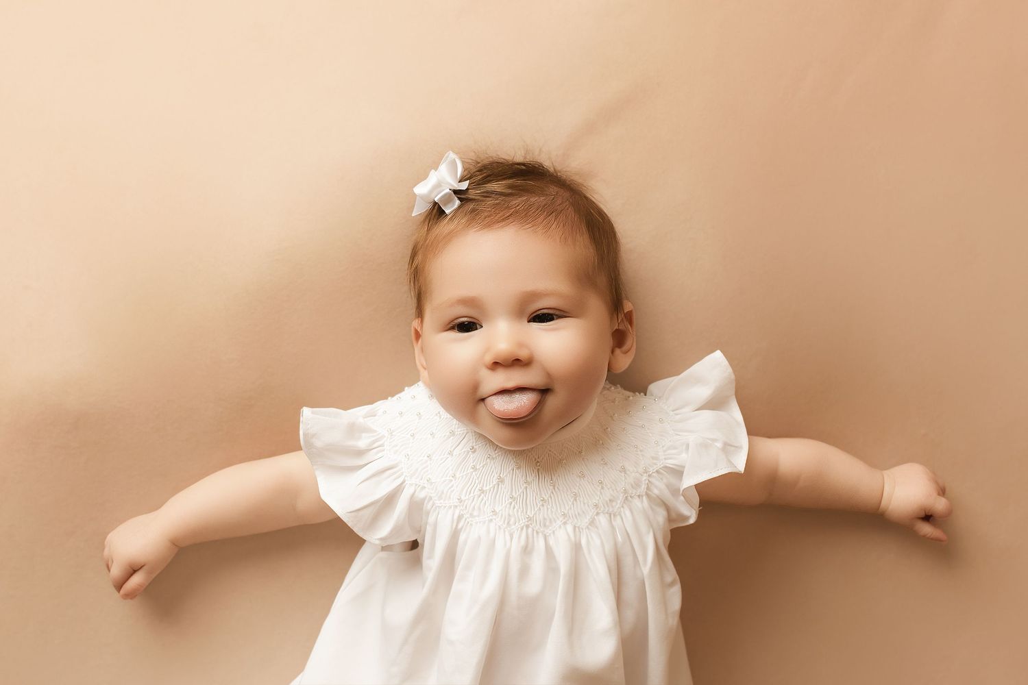 Baby wearing white lace dress photographed on beige background.