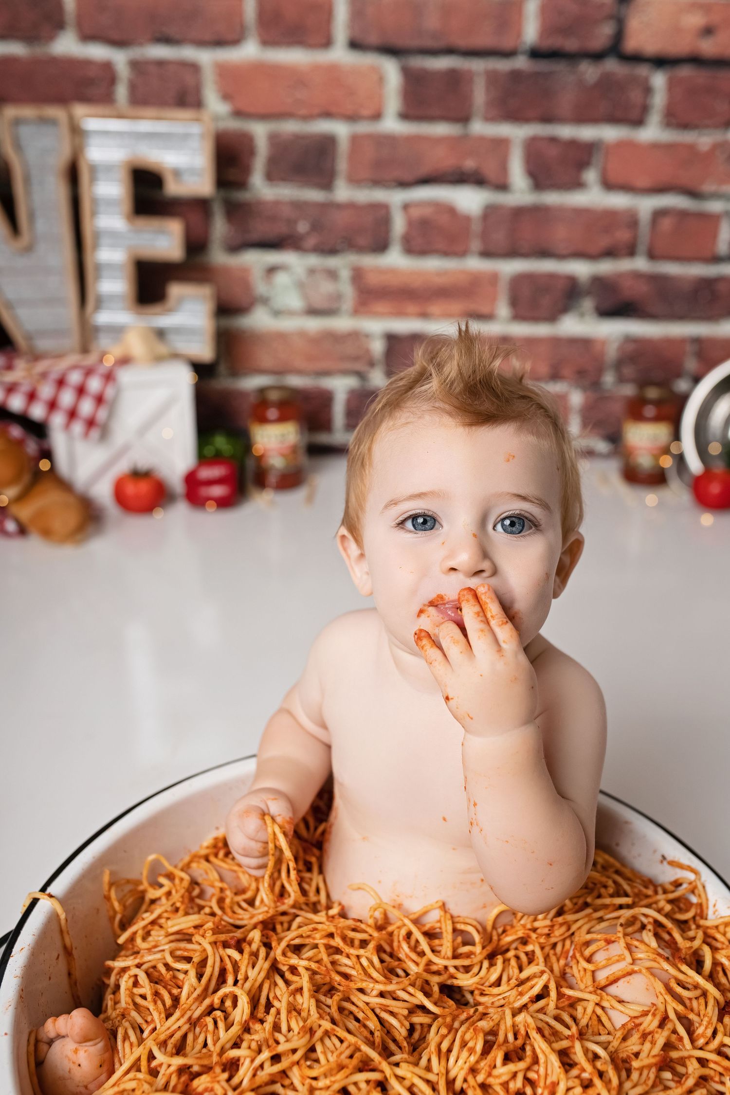 Creative baby photo with spaghetti pasta against rustic brick wall backdrop.