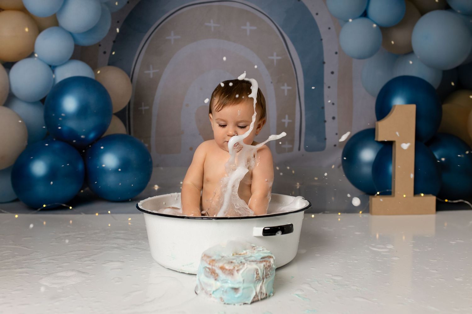 First birthday cake smash session with blue balloon arch and sparkle details.