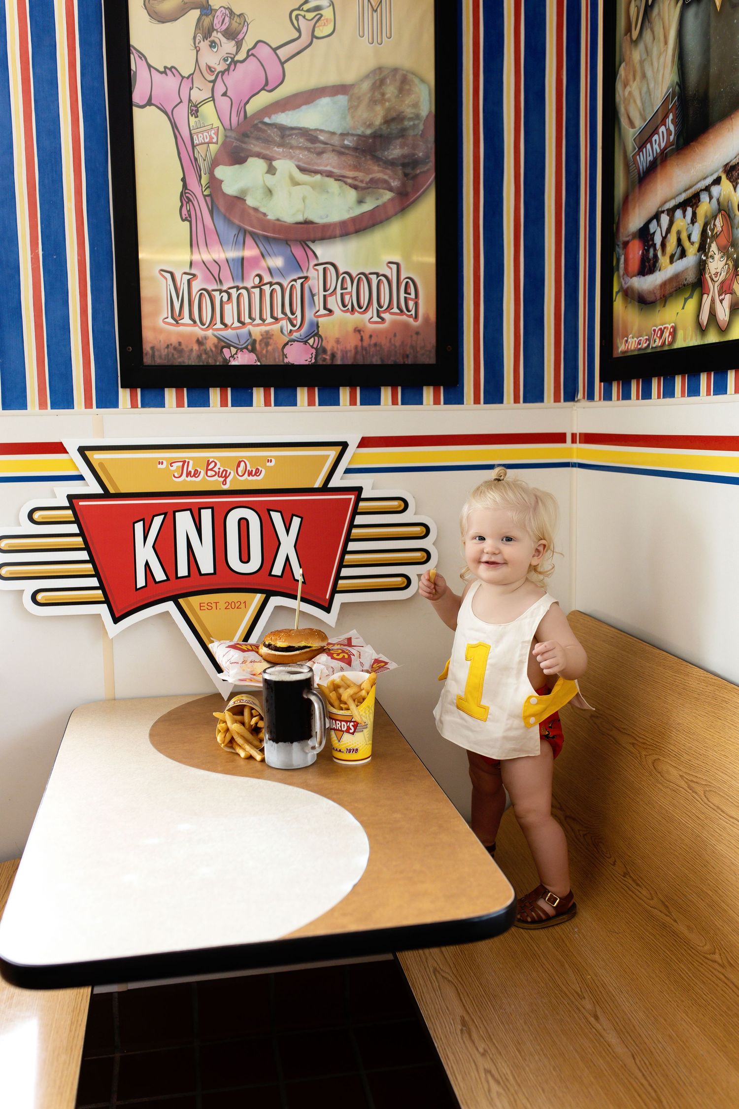 Baby sitting at retro diner booth with vintage decor and signage.